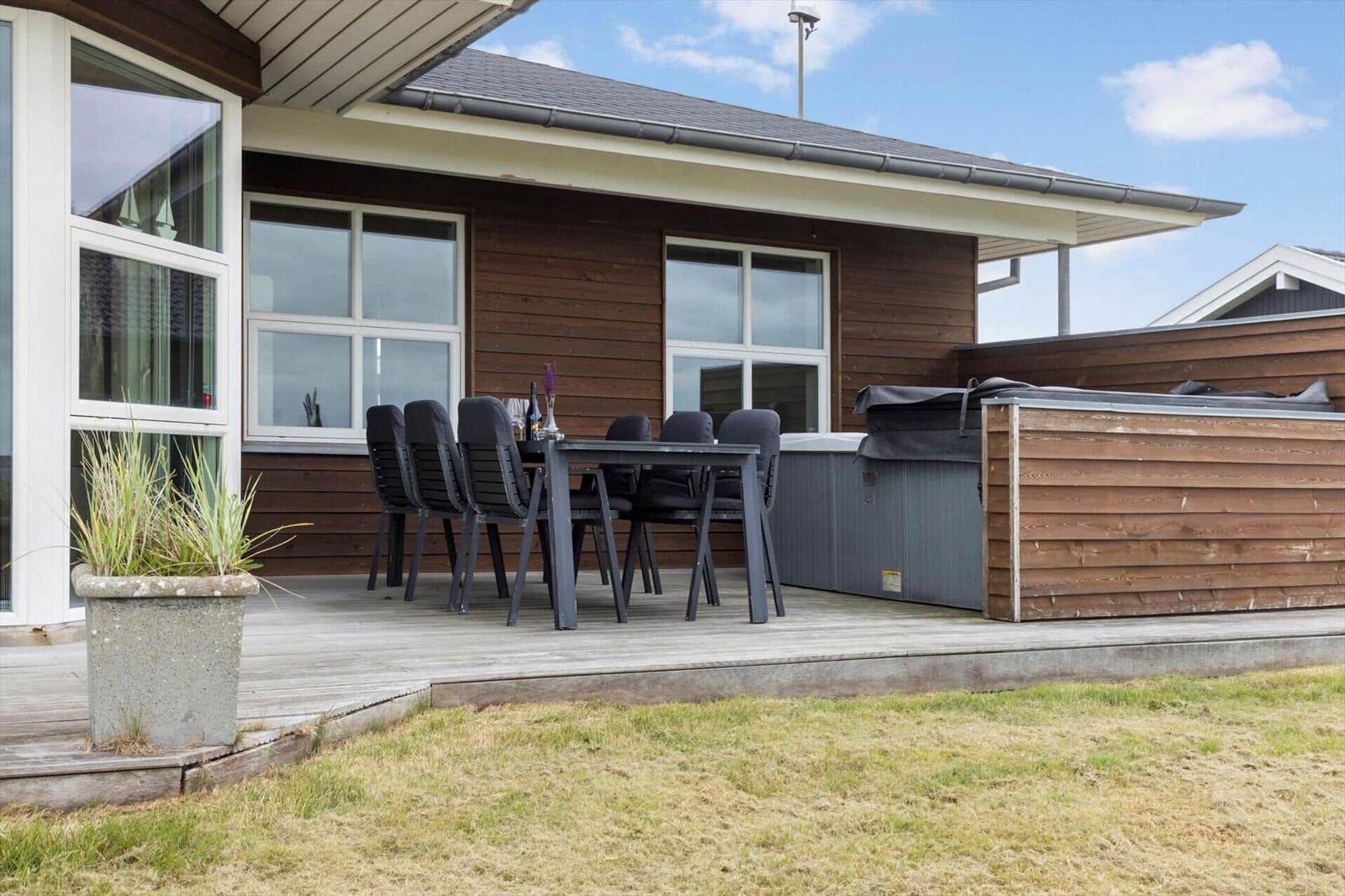 Terrasse mit Tisch, Stühlen und Whirlpool. Holzwand und Fenster sichtbar.