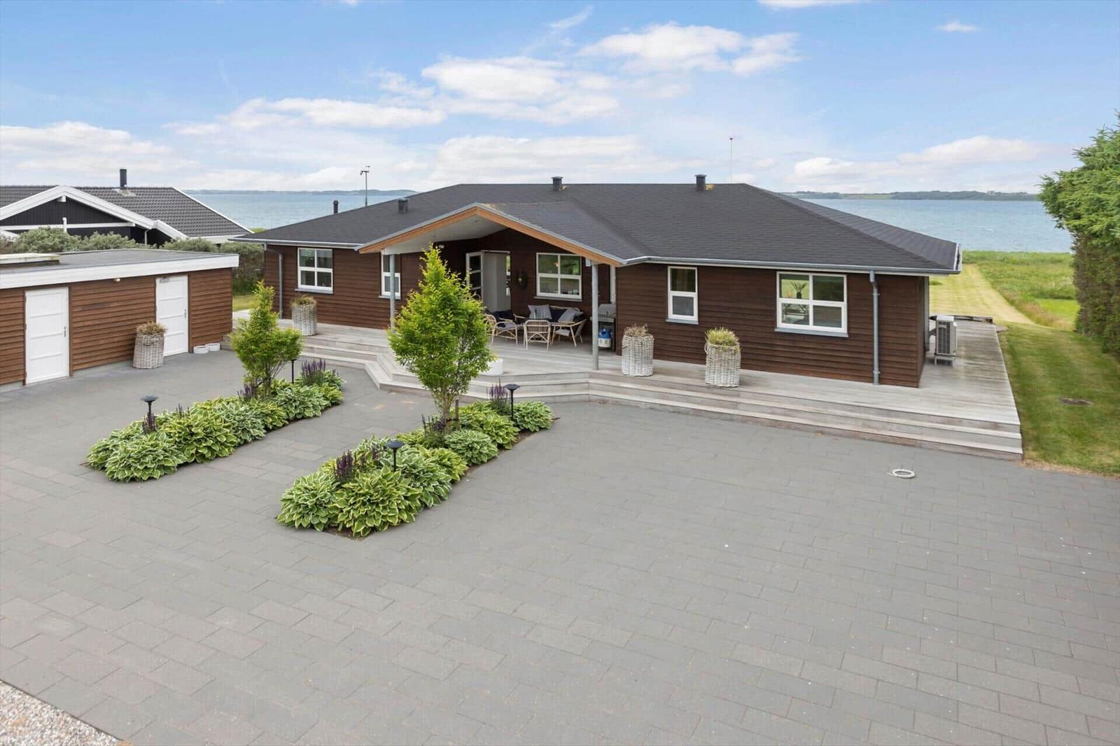 Ein Haus mit Terrasse und Blick aufs Wasser. Vorhof mit Pflanzen und Beete.