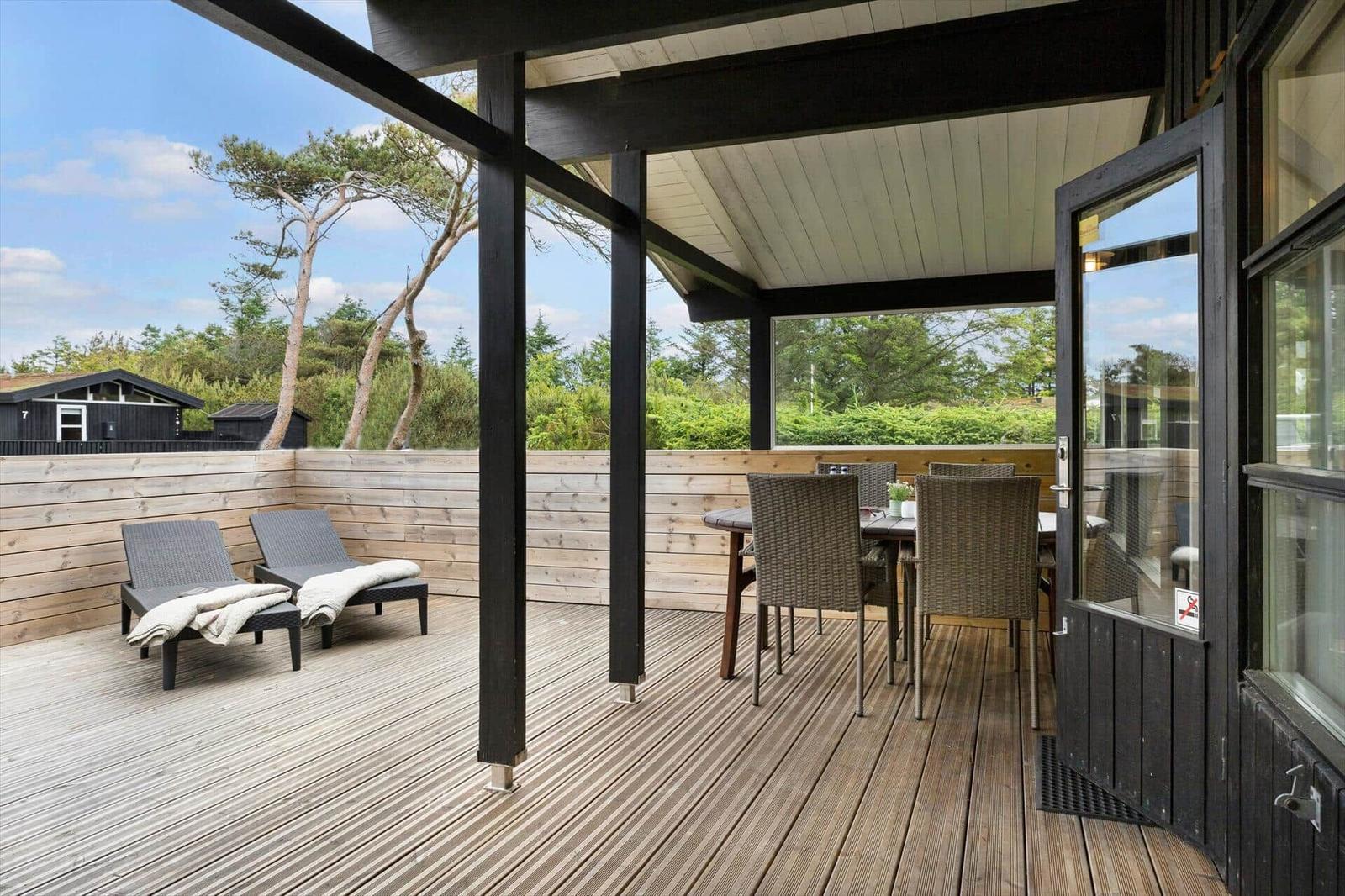 Terrasse mit Tisch, Stühlen und Liegen. Holzdecke und Sicht auf Bäume.