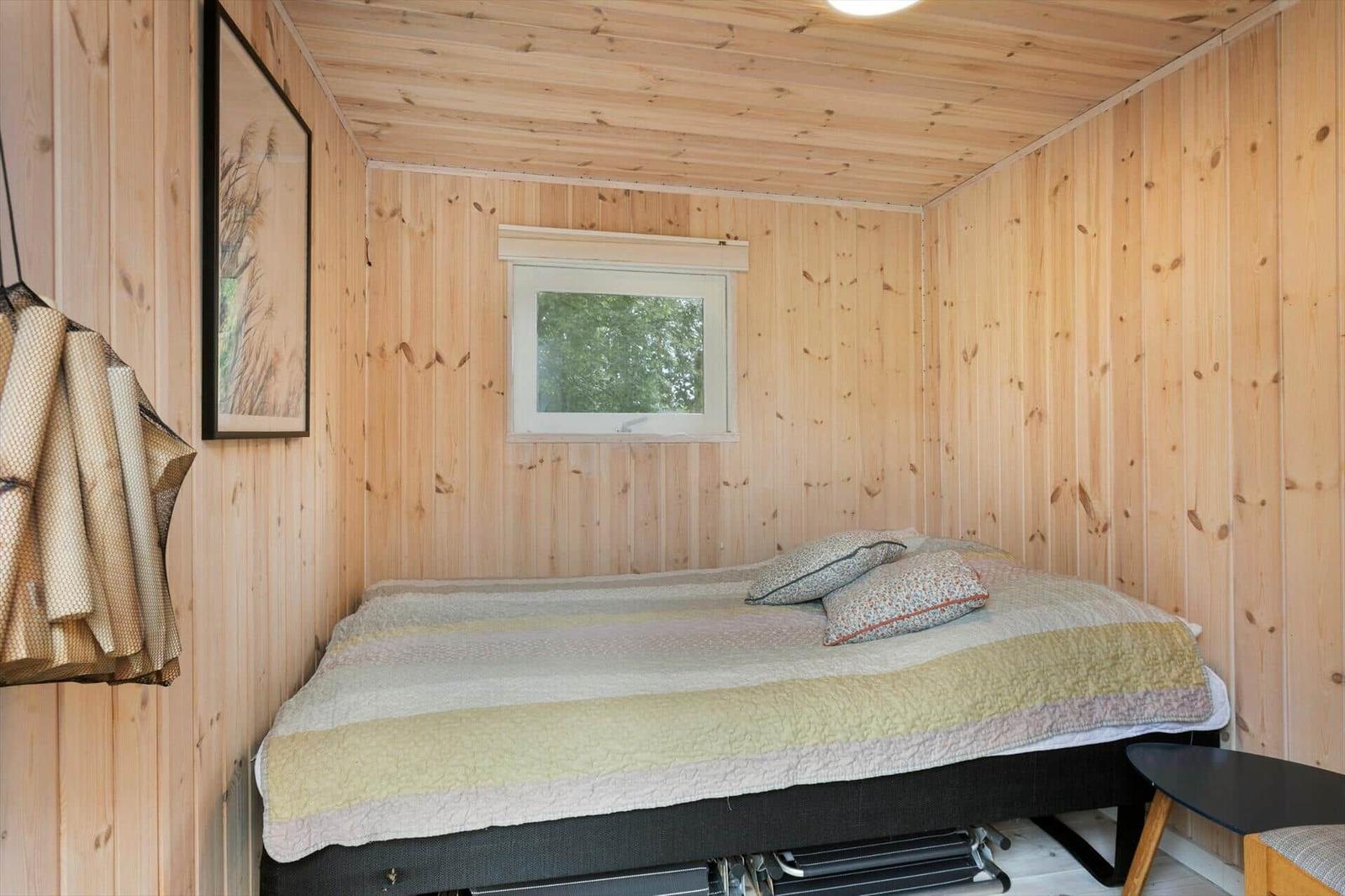 Schlafzimmer mit Holzwand, Bett und Fenster. Wandbild und Hängematte sichtbar.