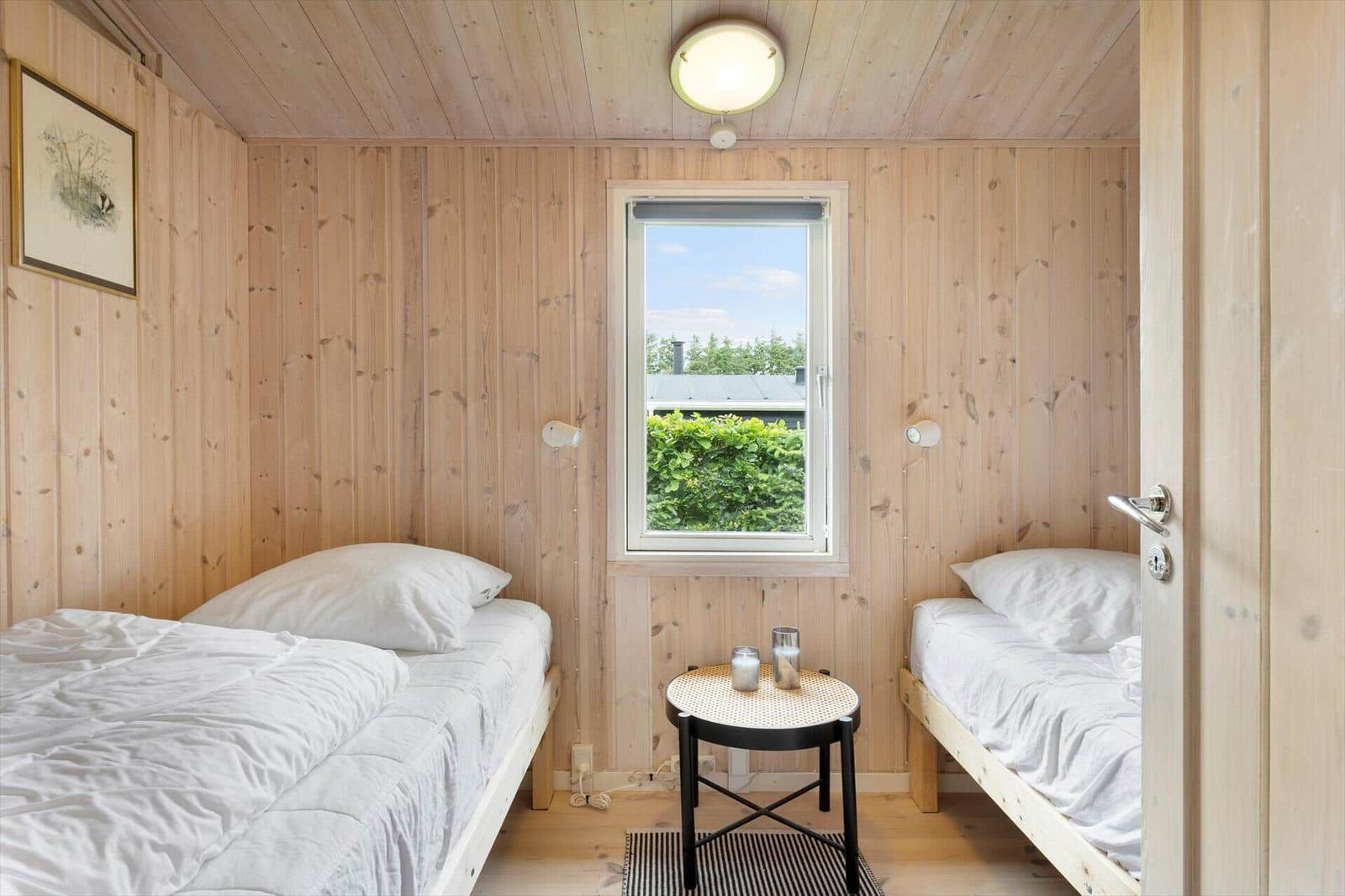 Zwei Betten in einem Holzraum mit Fenster und Tisch.