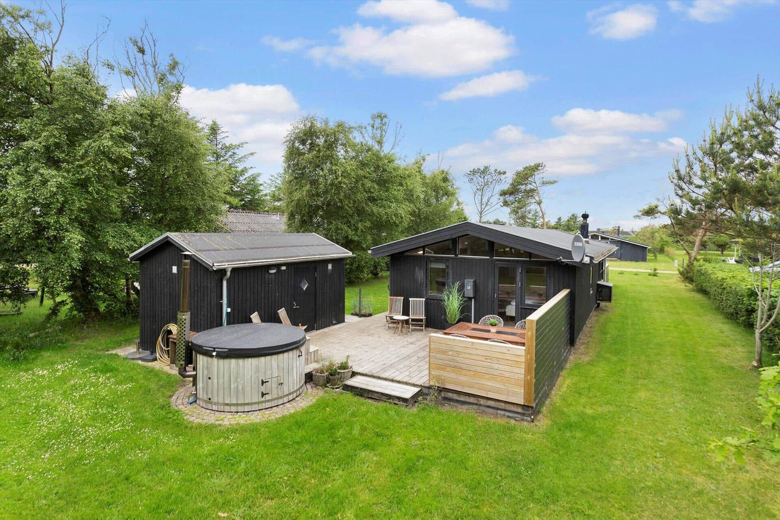 Schwarze Hütte mit Terrasse, Whirlpool und Garten. Blick auf den Himmel.