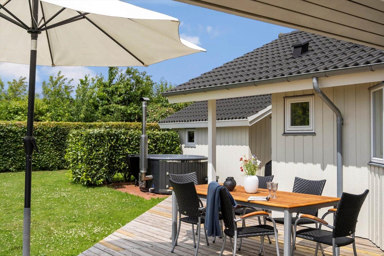 Deck with table, chairs, and umbrella. Backyard with hot tub and lawn.