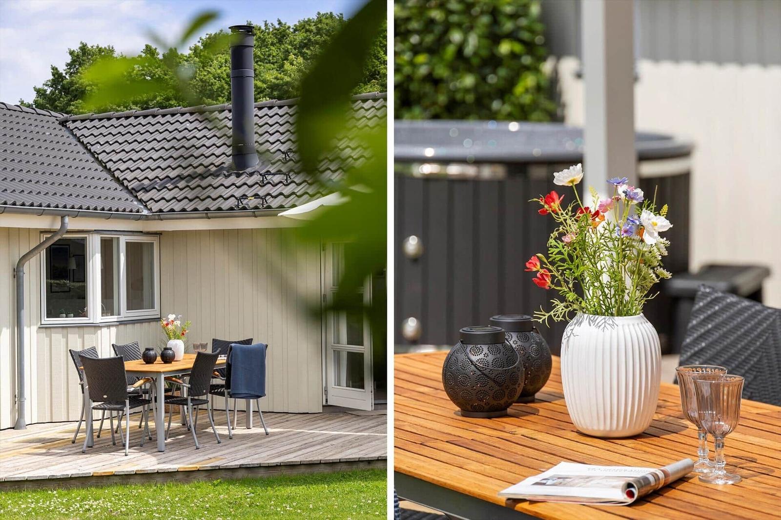 Deck with table, chairs, and flowers. Background: house with roof and grill.