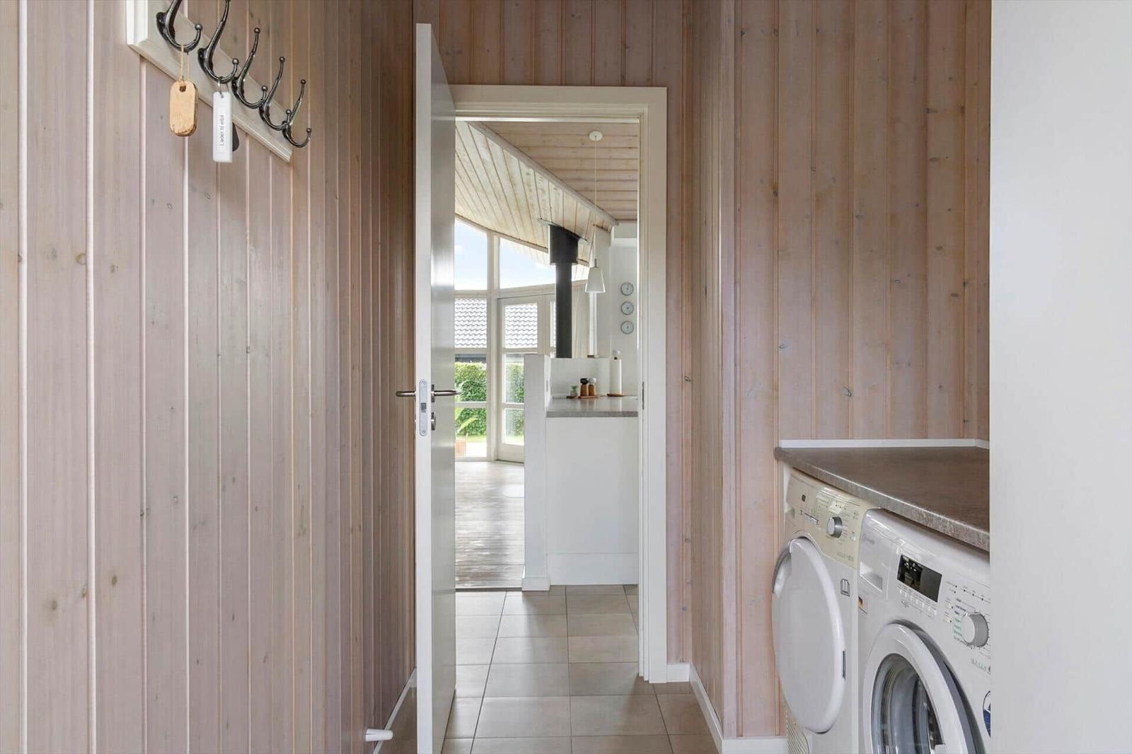House with wooden walls, washing machine, and view into the kitchen.