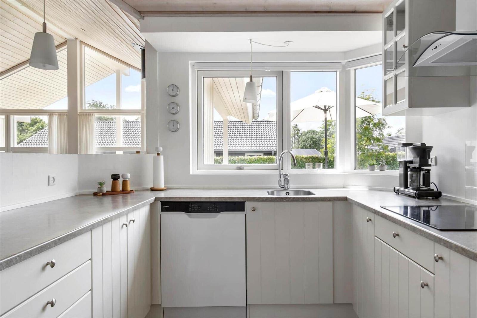 Kitchen with white cabinets, countertop, and garden view through windows