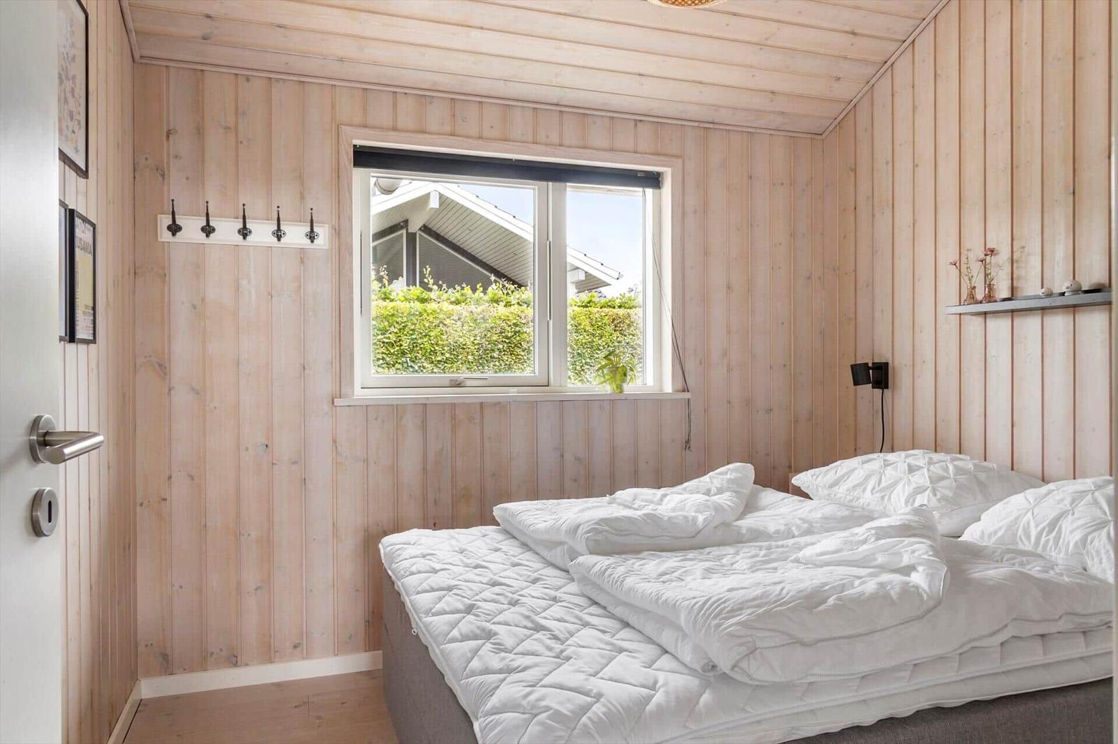 Bedroom with wooden walls, window, and bed with white bedding.