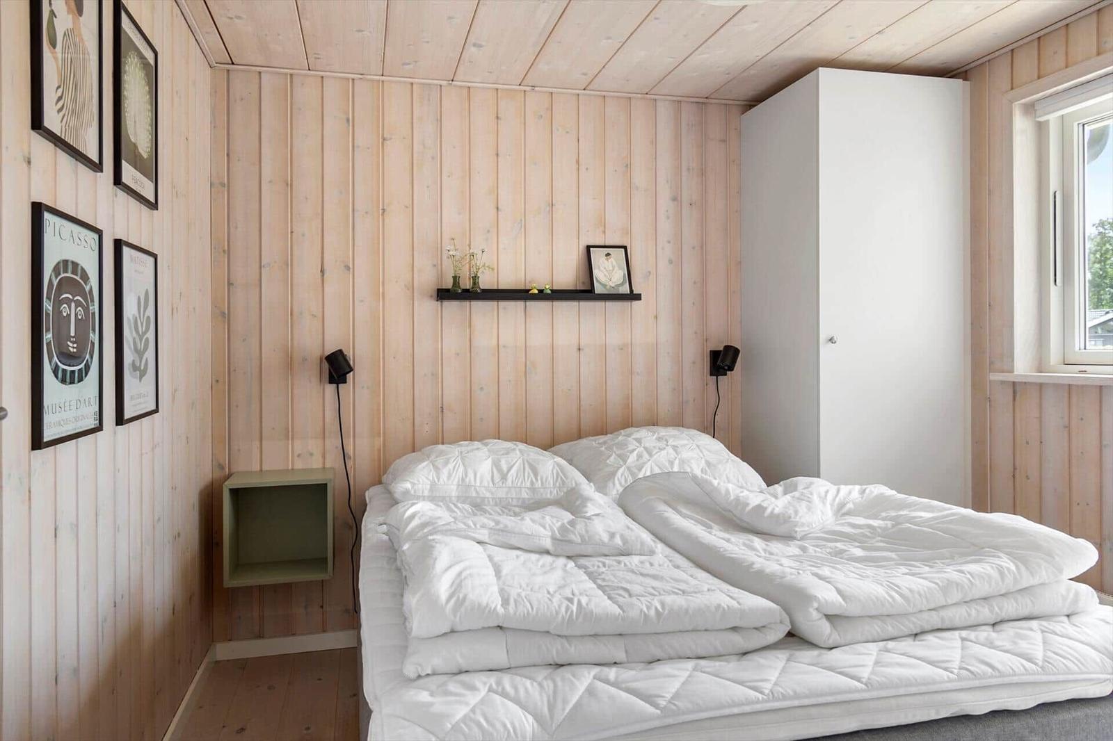 Bedroom with wooden walls, white bed, and wall art