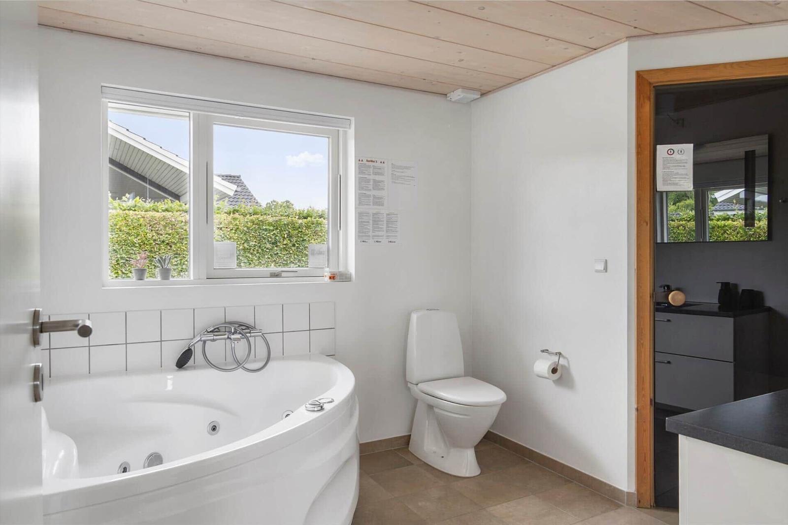 Bathroom with bathtub, toilet, and window overlooking the garden.
