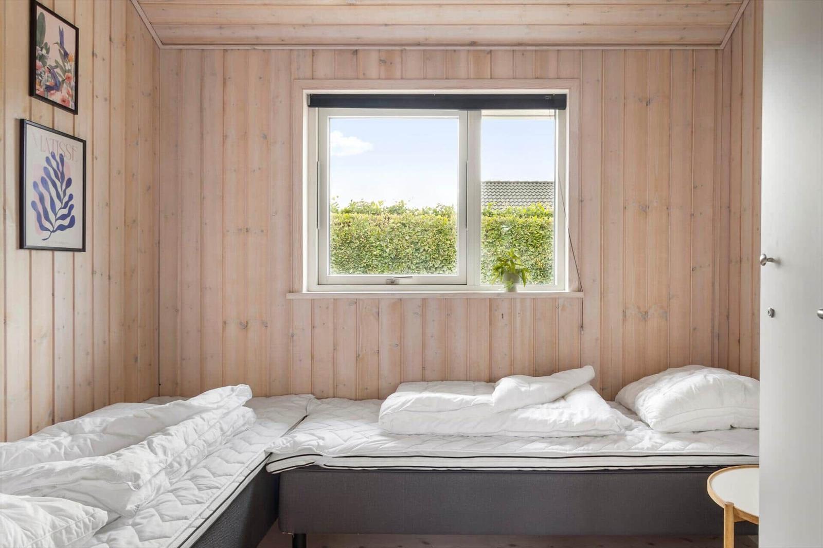 Bedroom with two mattresses, wooden walls, and view of greenery through window.