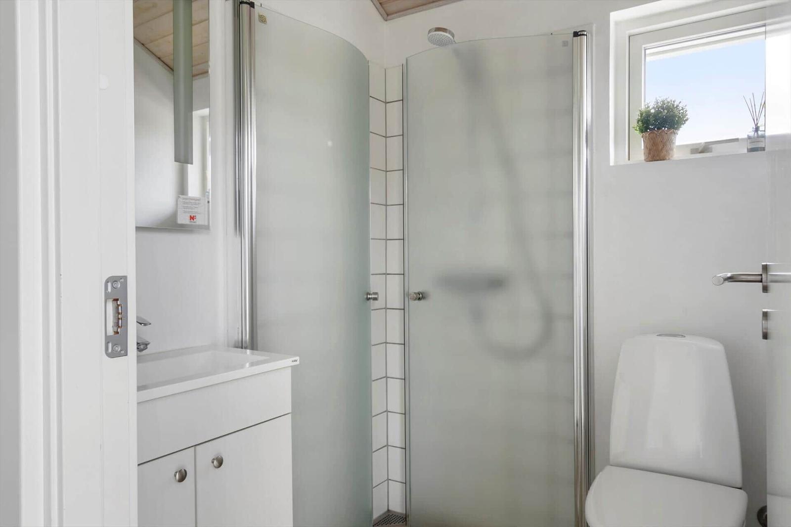 Bathroom with shower, sink, and toilet. Window with plant.