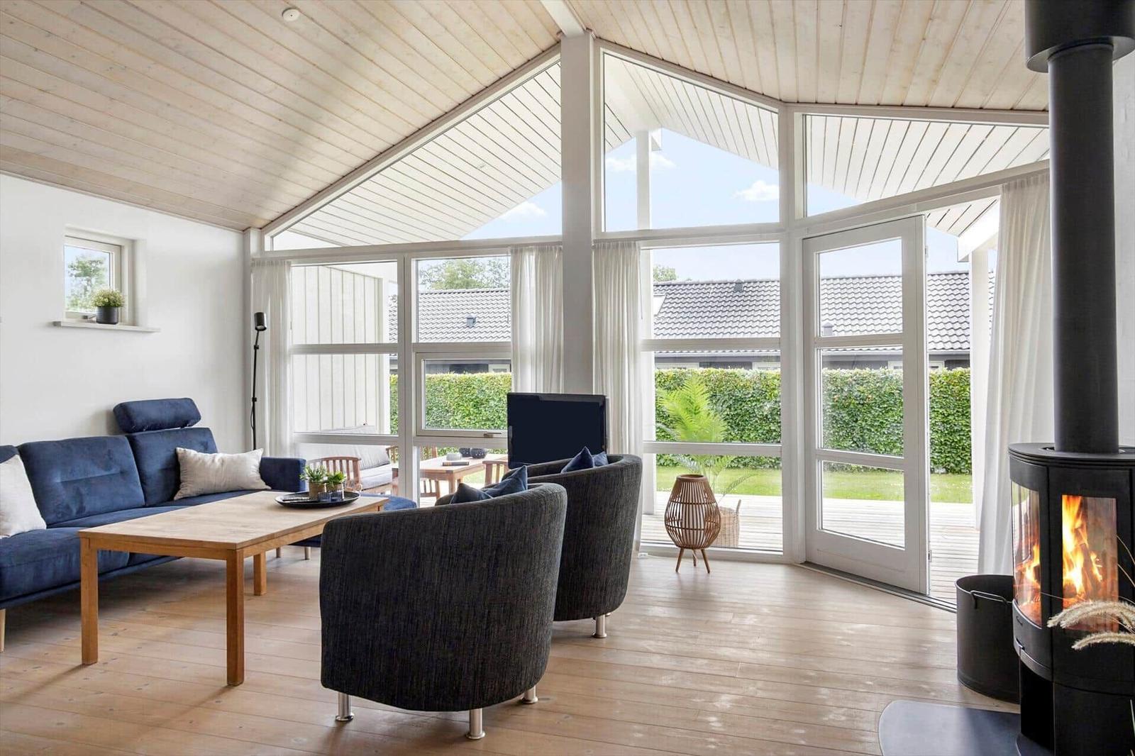 Living room with sofa, chairs, and fireplace. Large windows offer garden view.