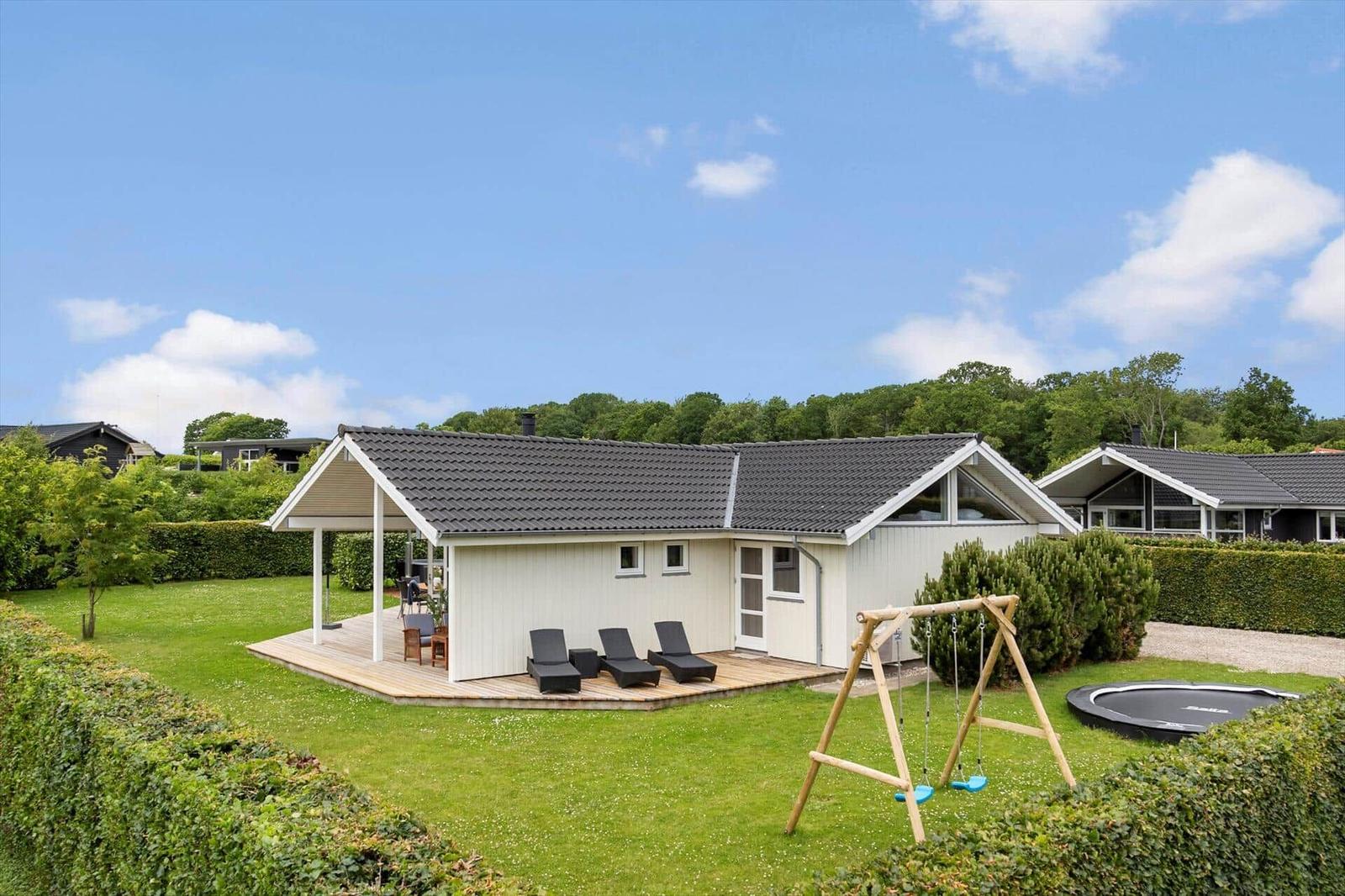 House with terrace, loungers, swing, and trampoline on a green lawn.