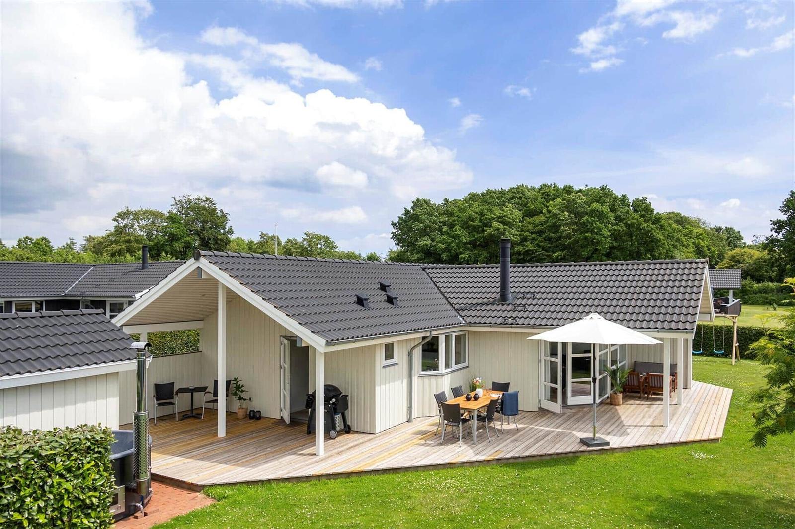 House with terrace, grill, and garden. White facade, dark roof tiles.