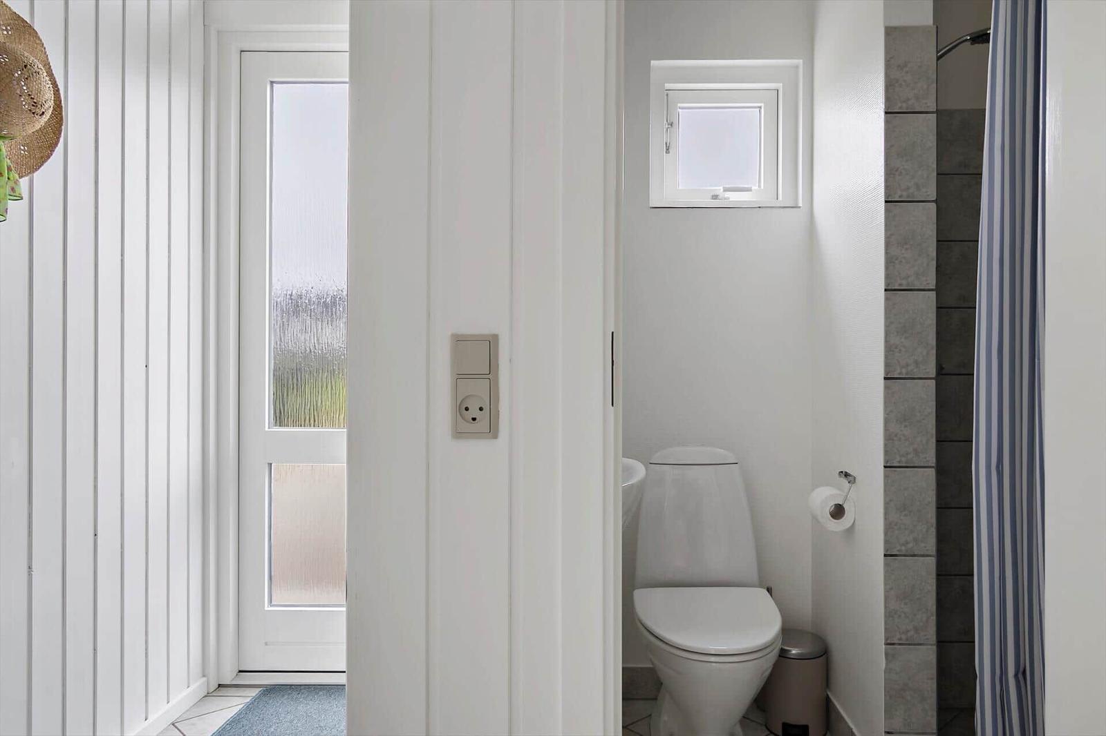 Bathroom with toilet, shower, and window. White walls and gray tiles.