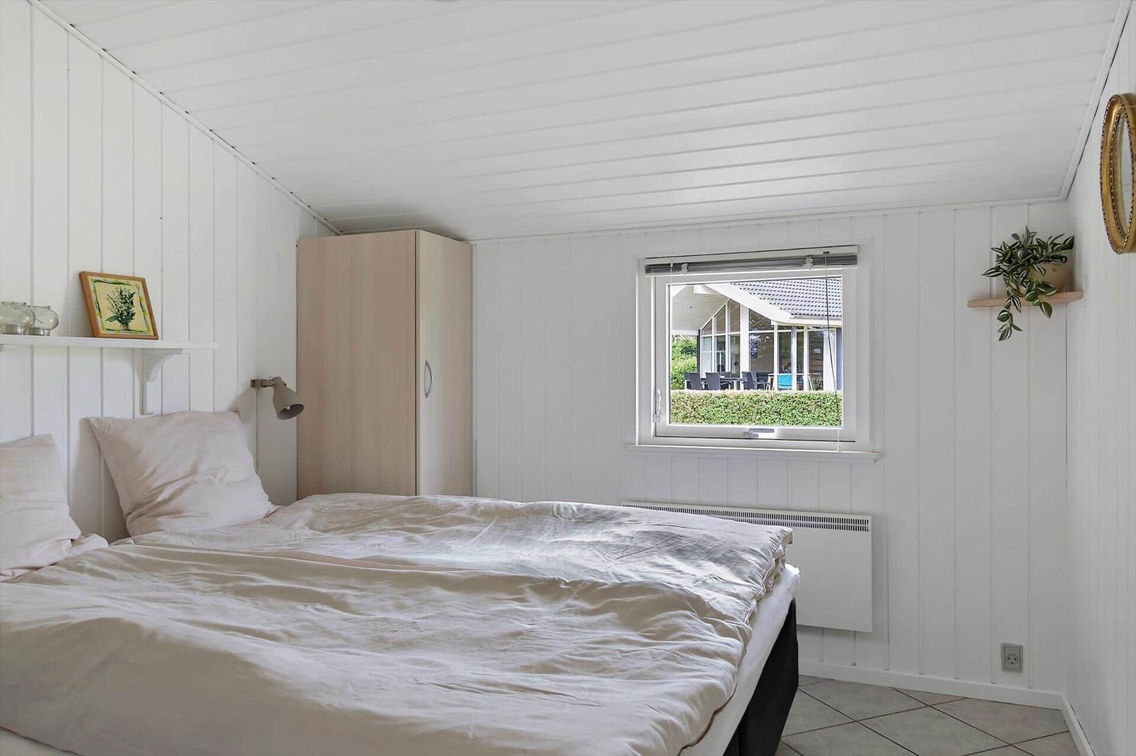 Bedroom with bed, wardrobe, and view of garden through window.
