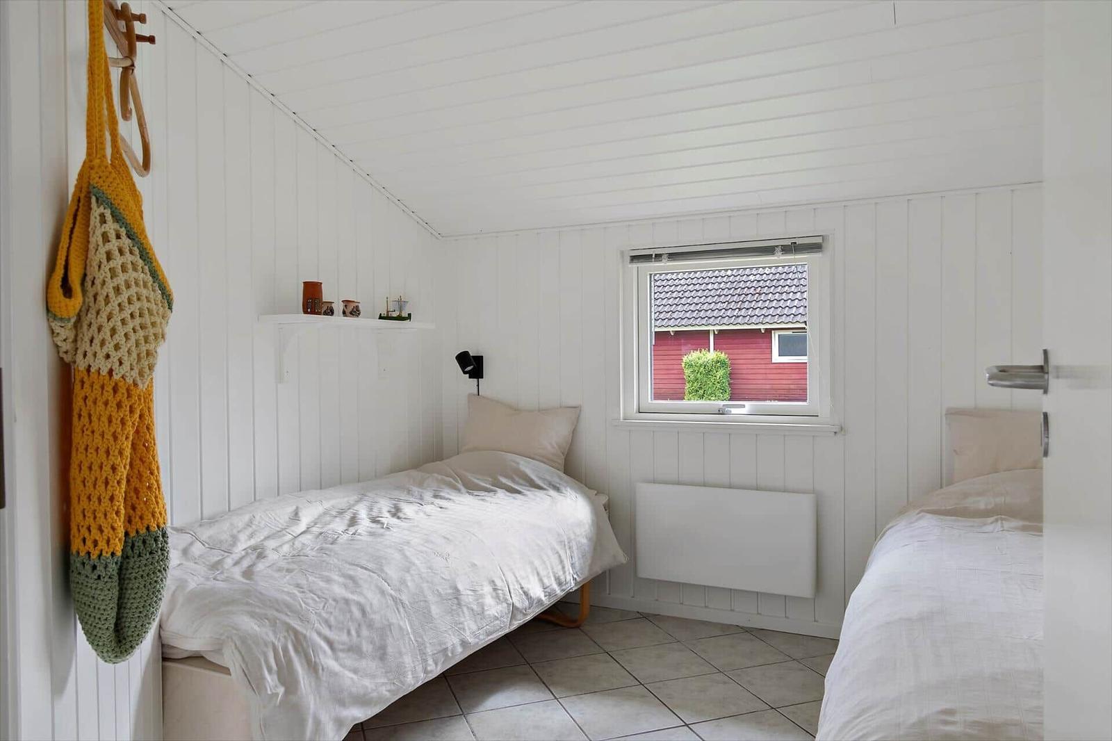 Two single beds, white paneled walls, window with view of red house.