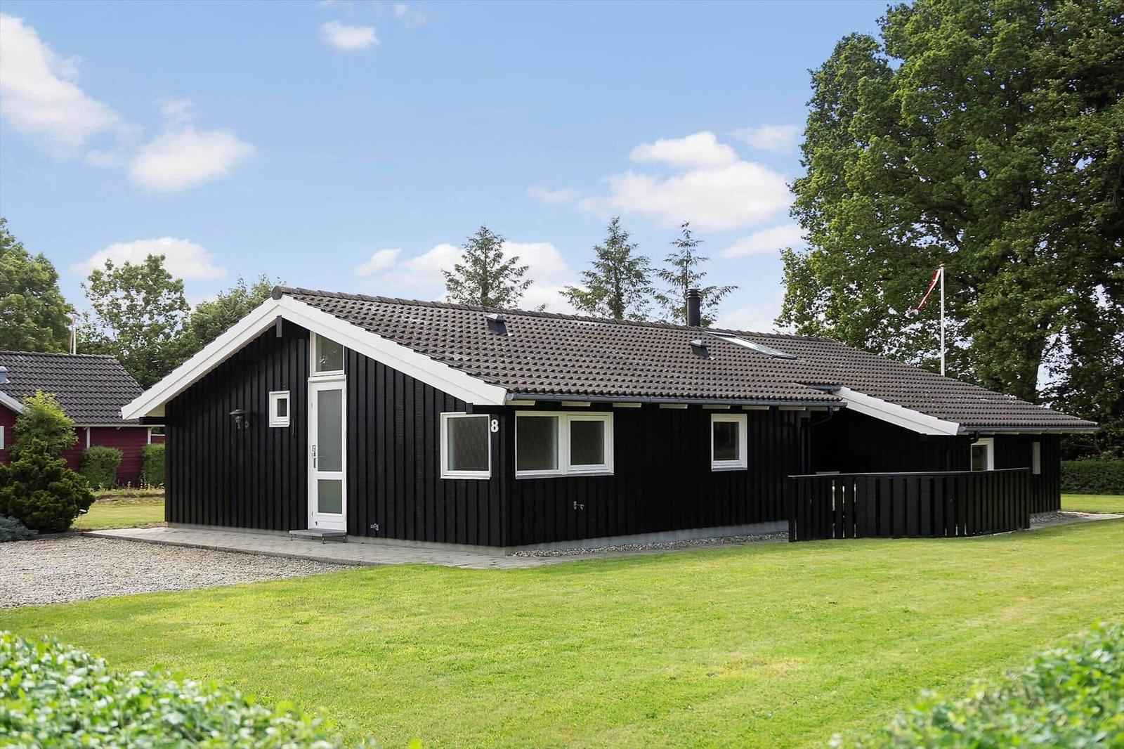 Black wooden house with white window frames and terrace. Green lawn and trees surround the house.