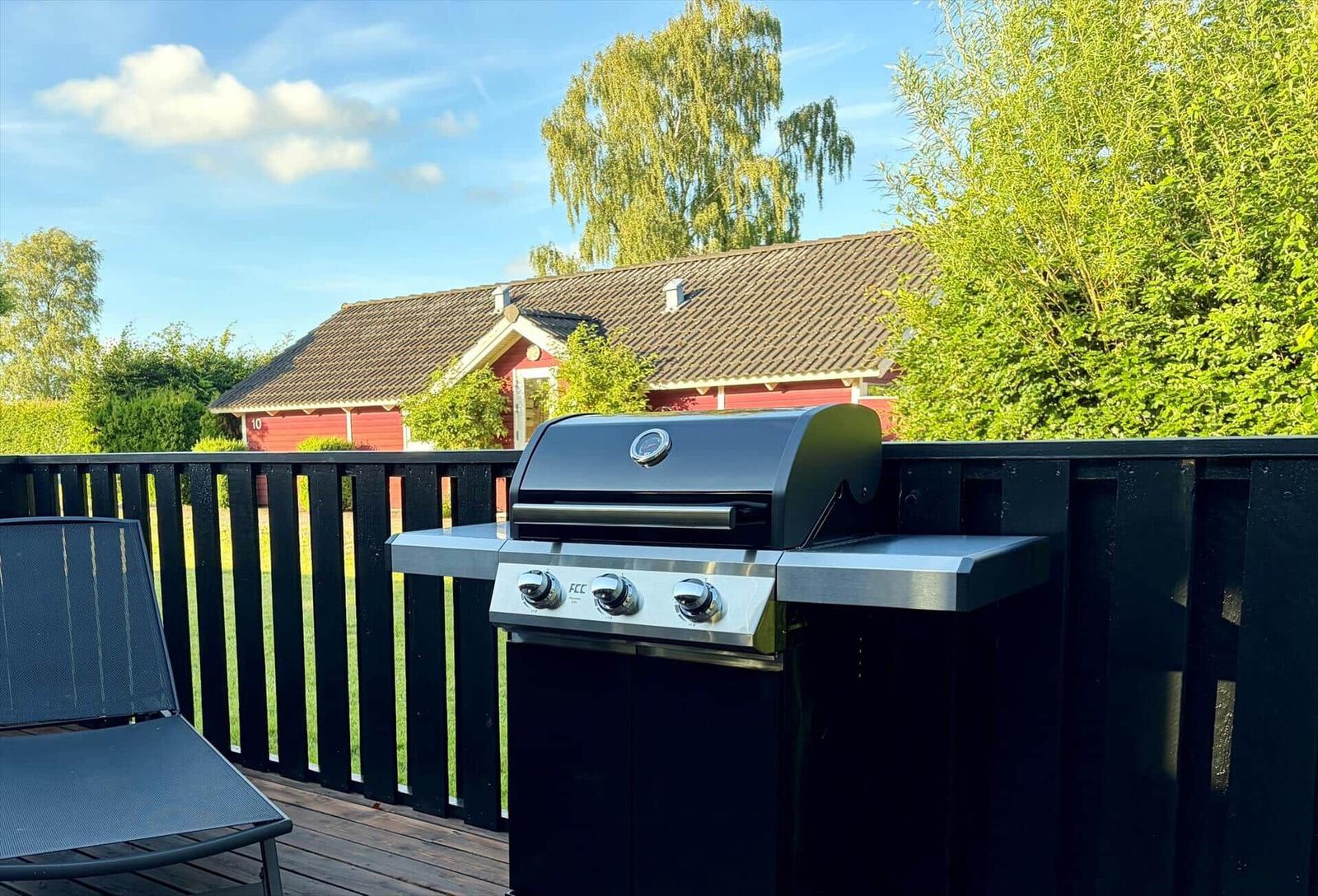 Gas grill on terrace with view of red house and green areas.