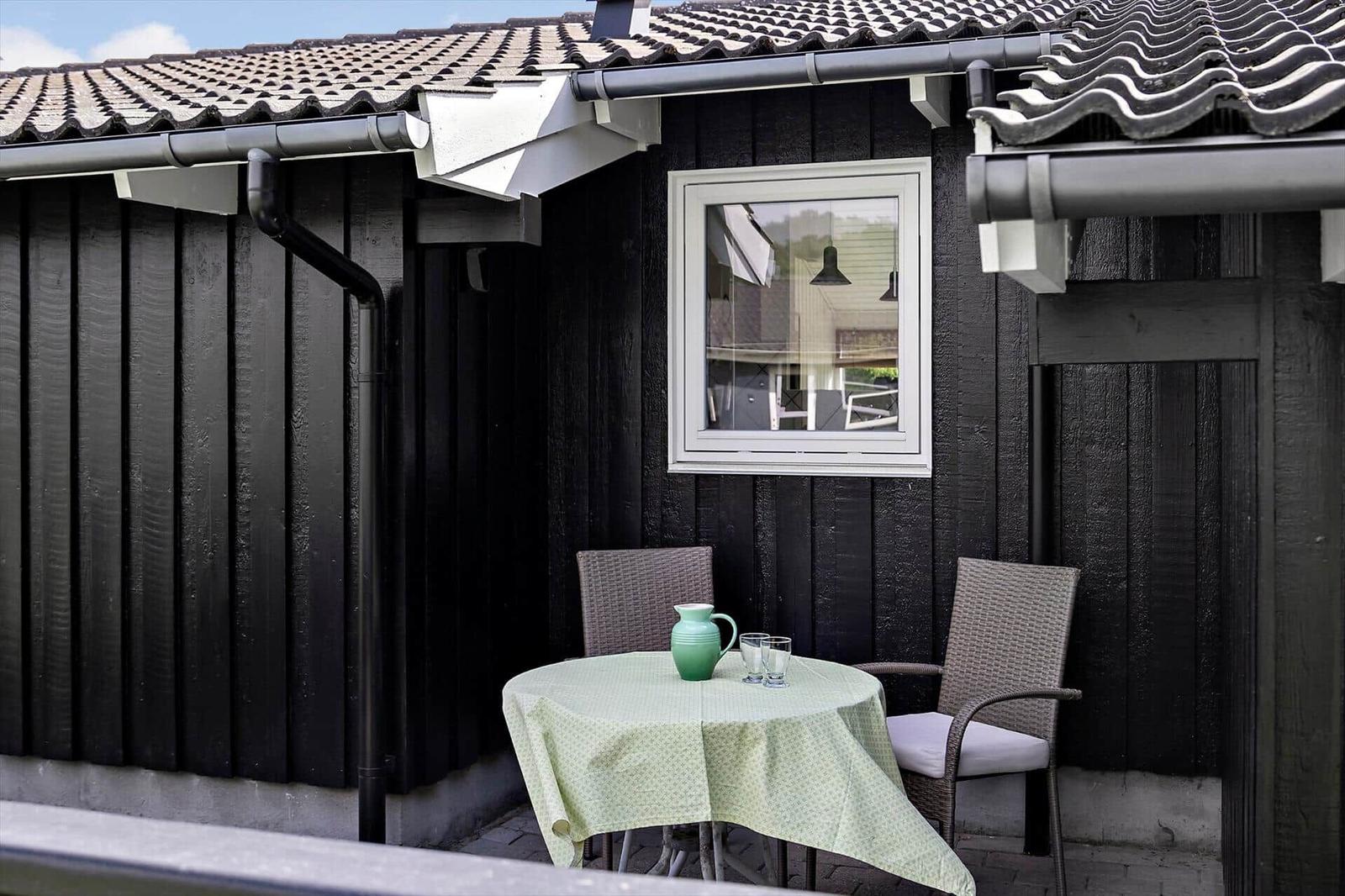 Outdoor terrace with table, two chairs, and green tablecloth. Black wooden wall and window.