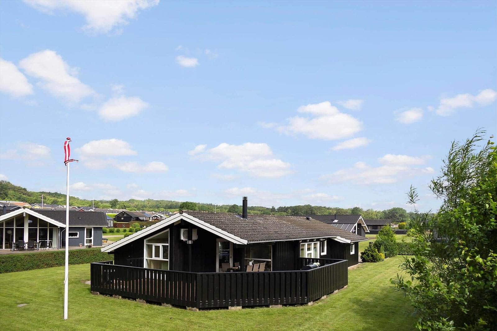Black holiday house with terrace and garden under blue sky with white clouds.