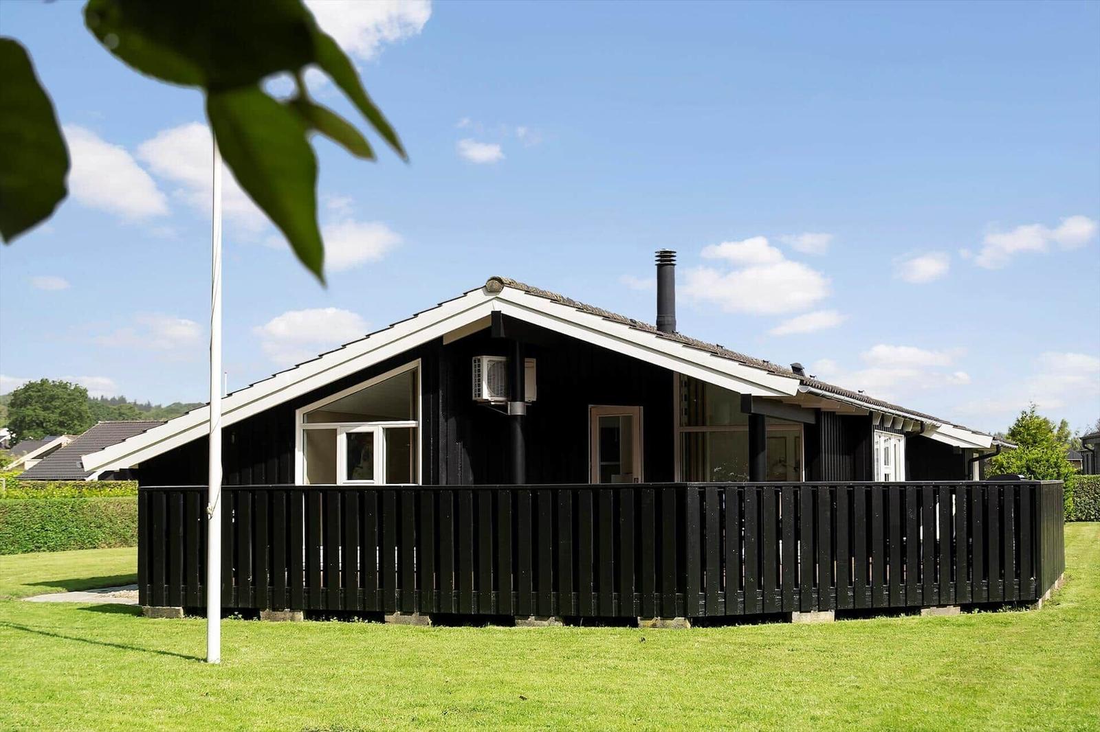 Black wooden house with balcony and grill area on green lawn under blue sky.