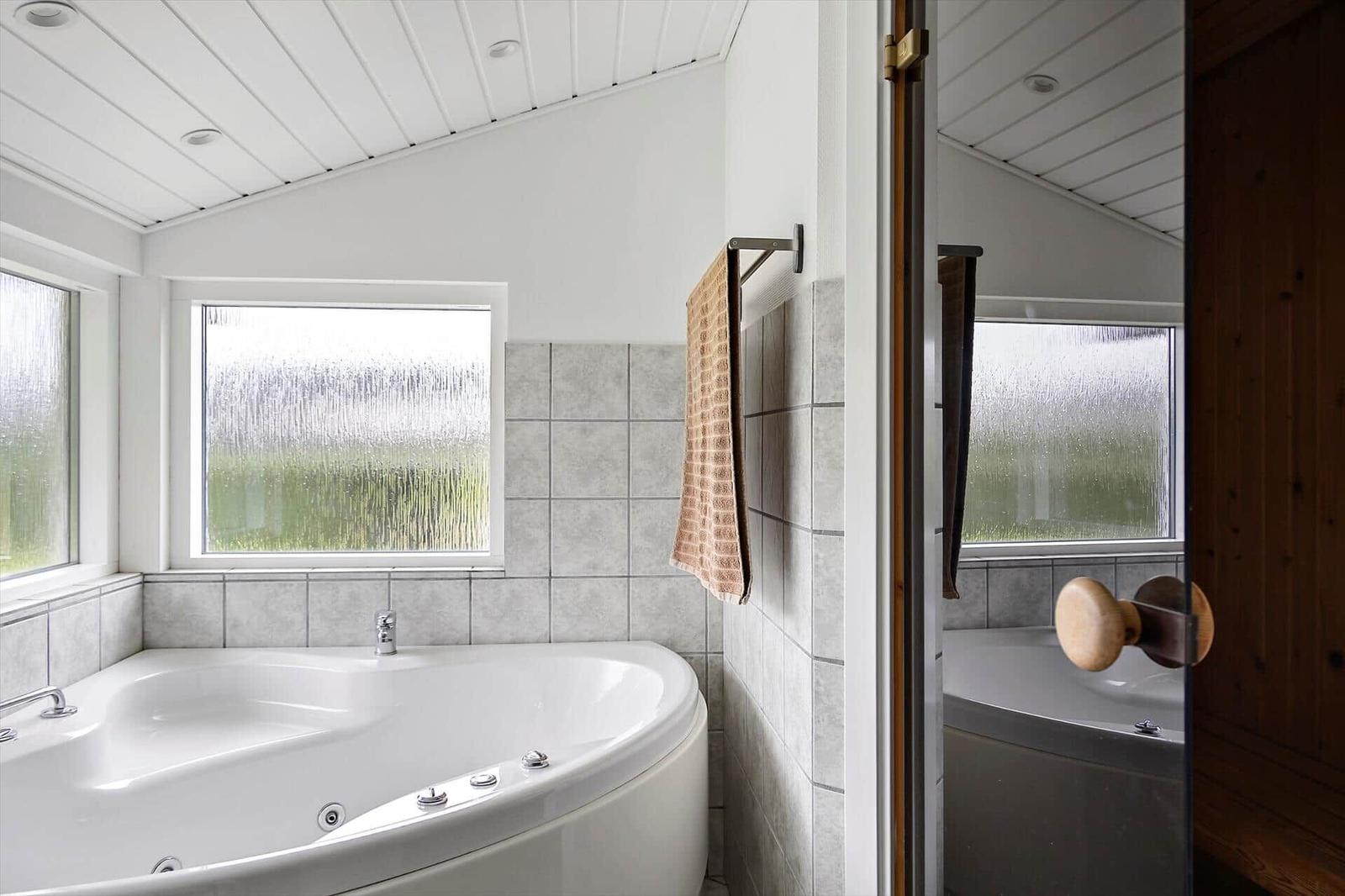 Bath with whirlpool, frosted glass window, and wooden door.