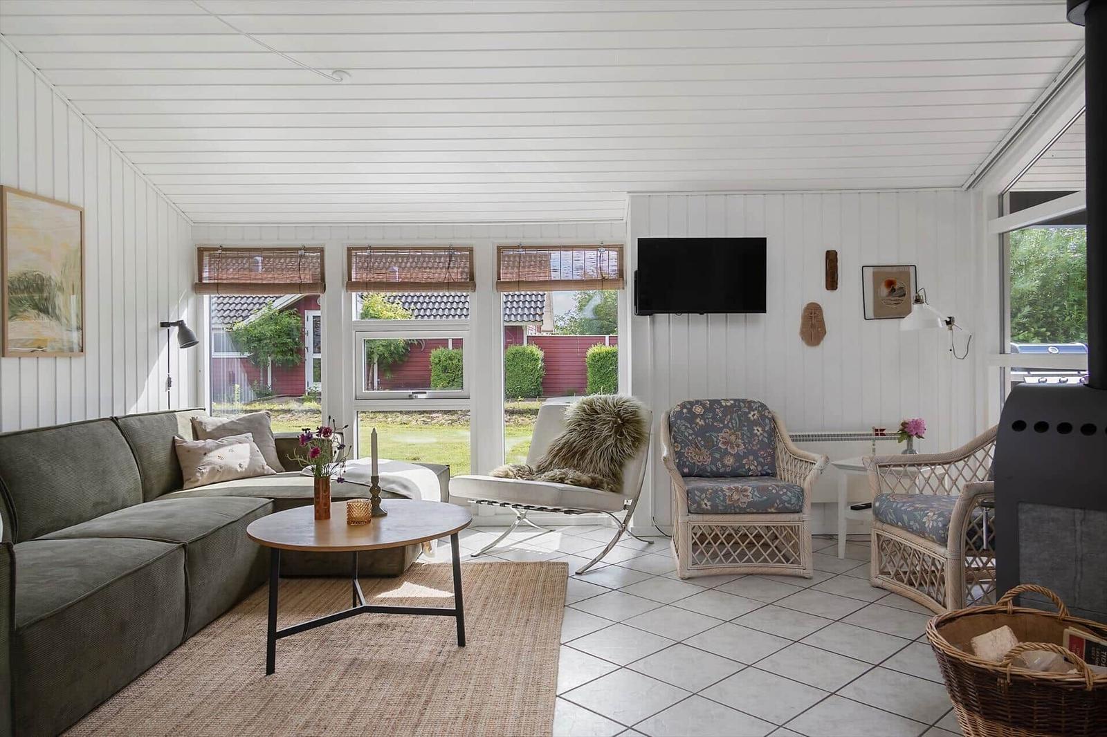 Living room with sofa, chairs, and TV. Windows overlook the garden.