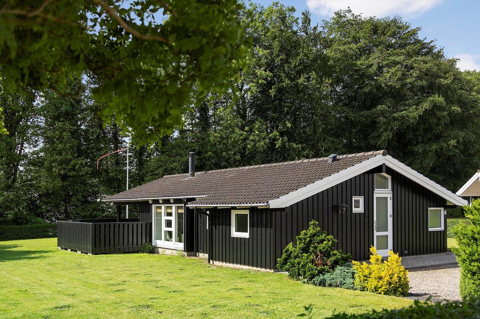 Black wooden house with white roof trim, surrounded by grass and trees.