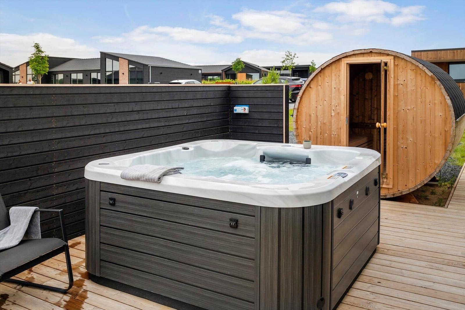 Außenwhirlpool mit Sauna auf Holzterrasse. Schwarze Holzwand im Hintergrund.