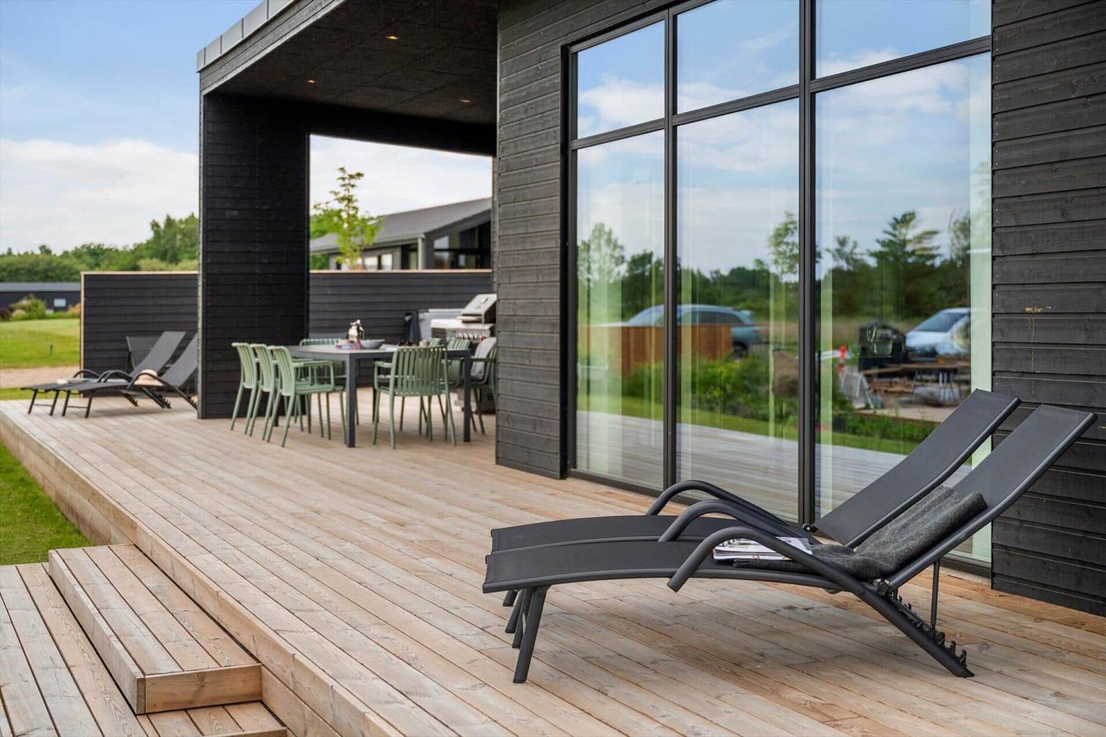 Terrasse mit Loungemöbeln, Tisch und Stühlen. Glasfront und Holzwände.