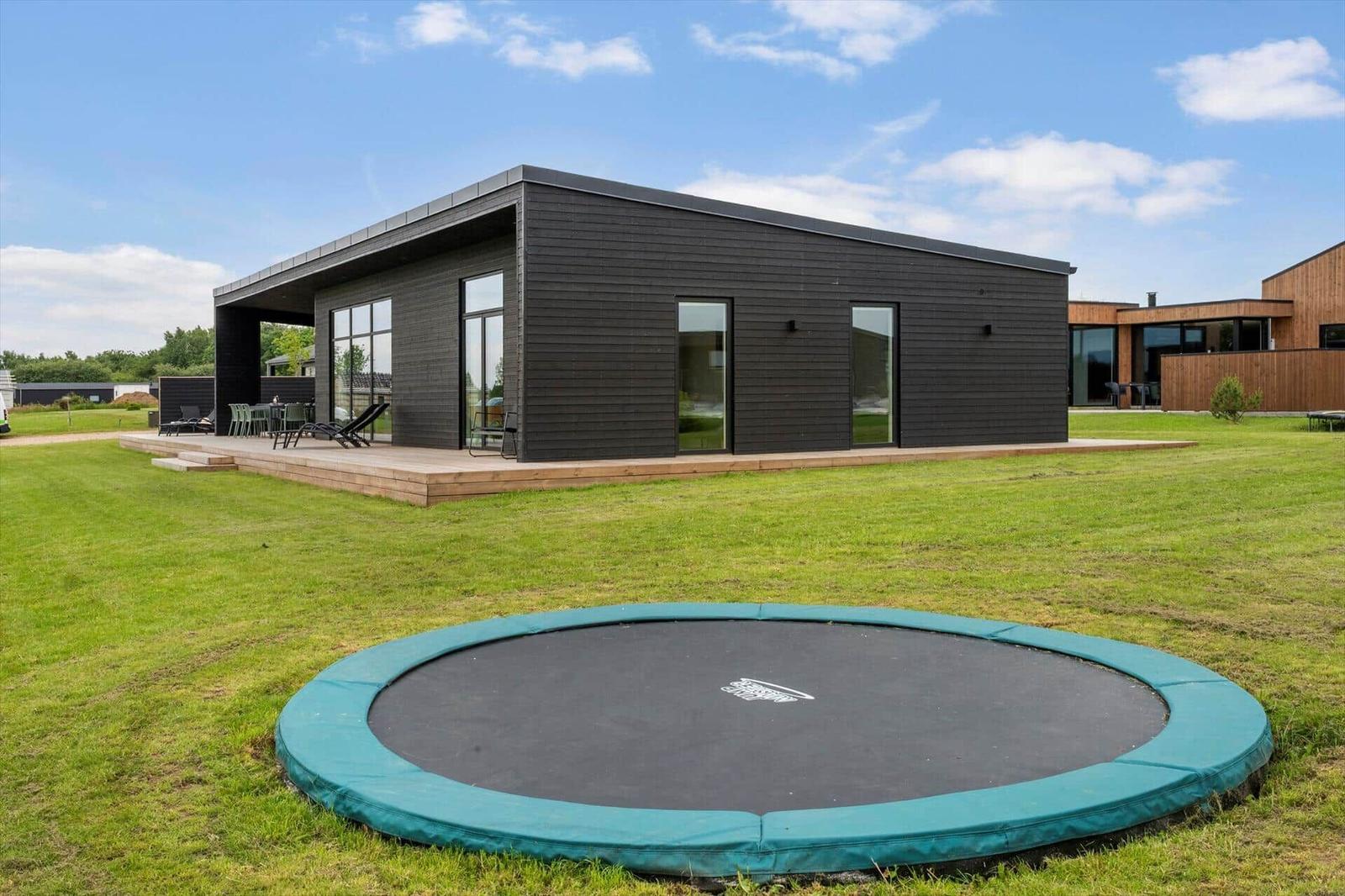Moderne Villa mit Terrasse und Trampolin auf grünem Grundstück.