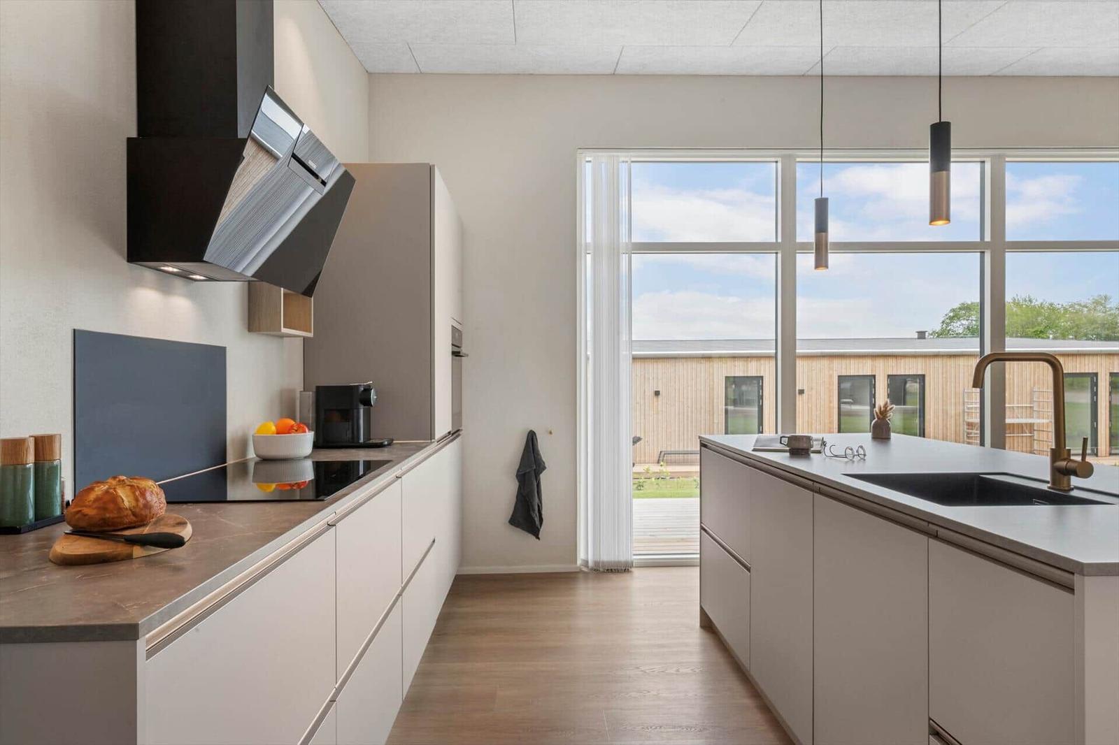 Moderne Küche mit Kücheninsel, großen Fenstern und Blick auf Außenbereich.