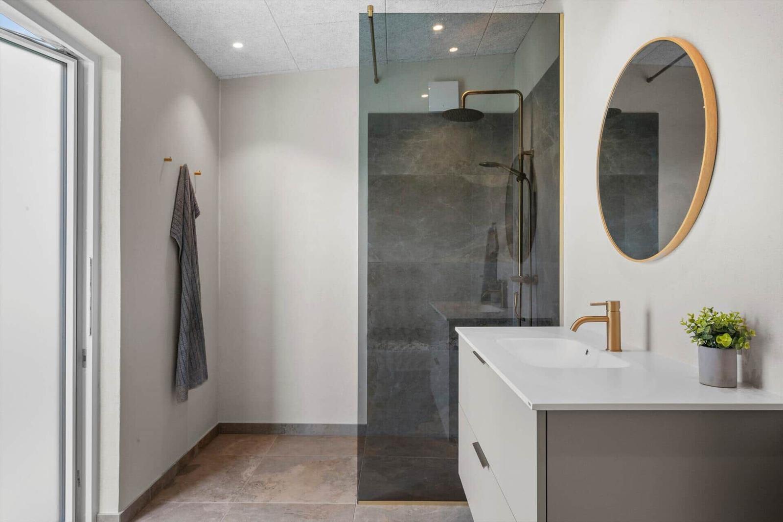 Moderne Dusche mit Glaswand, Waschtisch mit Spiegel und Handtuchhalter an der Wand.