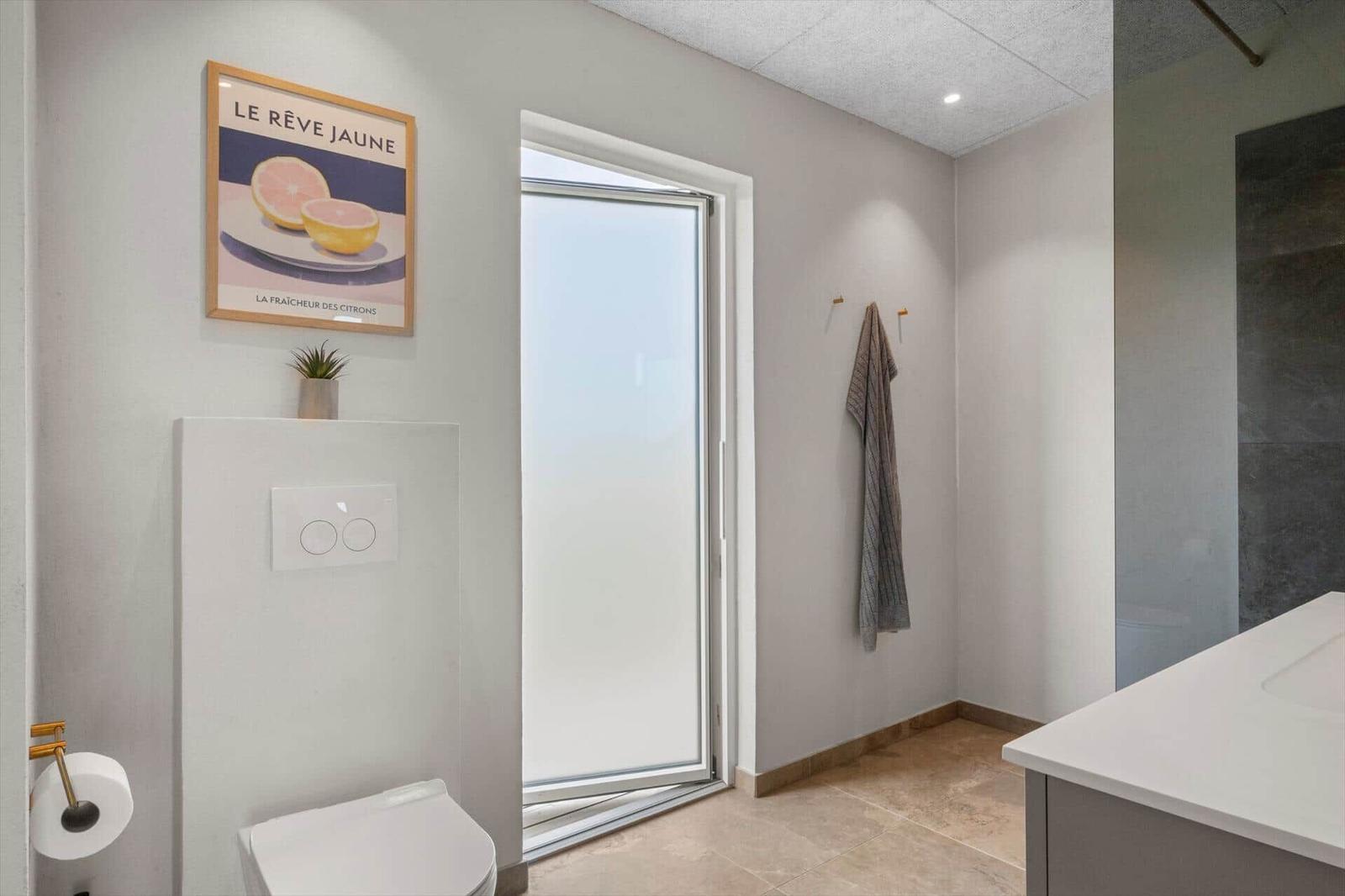 Badezimmer mit Toilette, Spiegel und Dusche. An der Wand hängt ein Bild mit Zitronenmotiv.