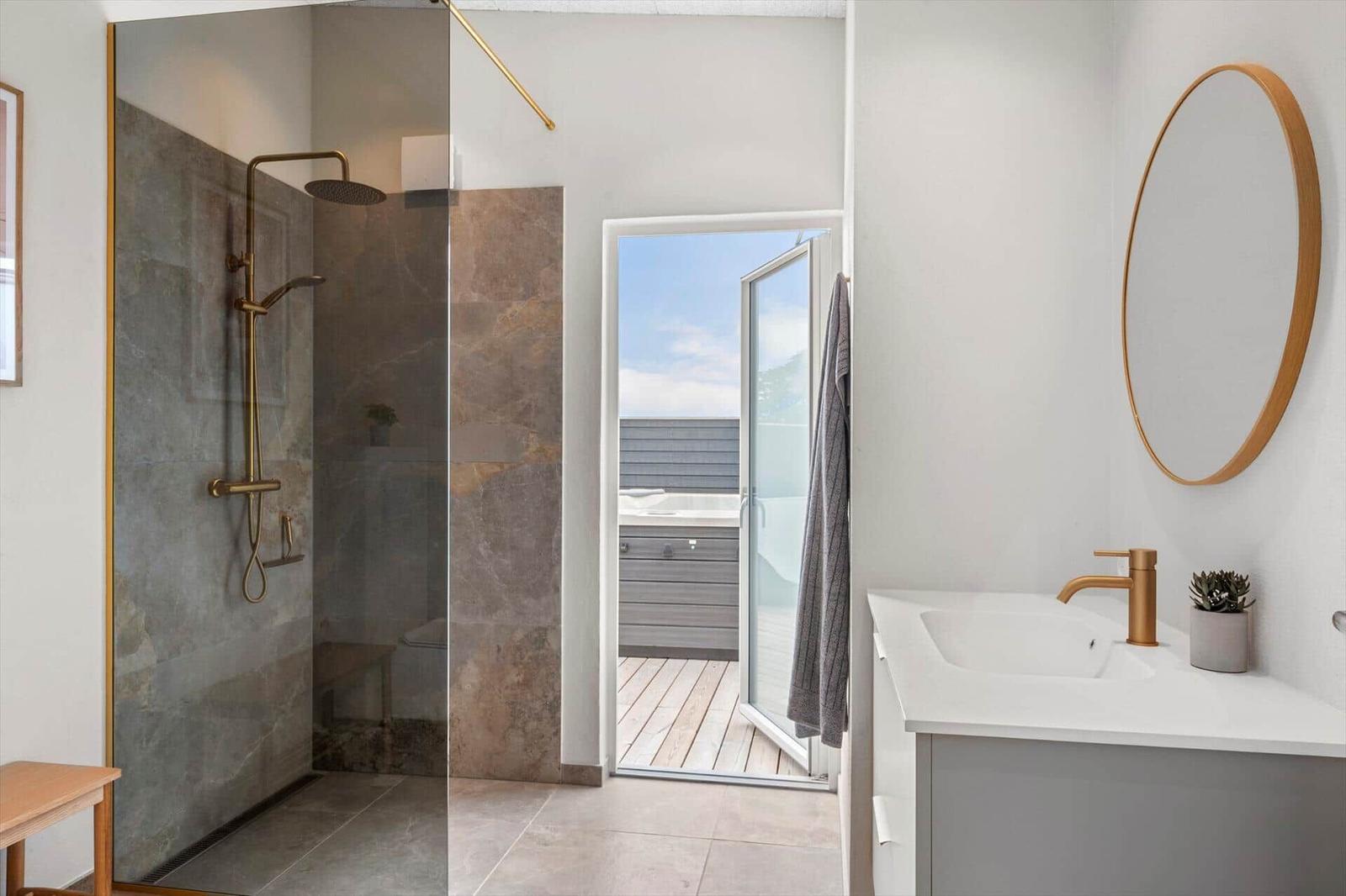 Dusche mit Glaswand, Waschbecken und Blick auf die Terrasse mit Whirlpool.