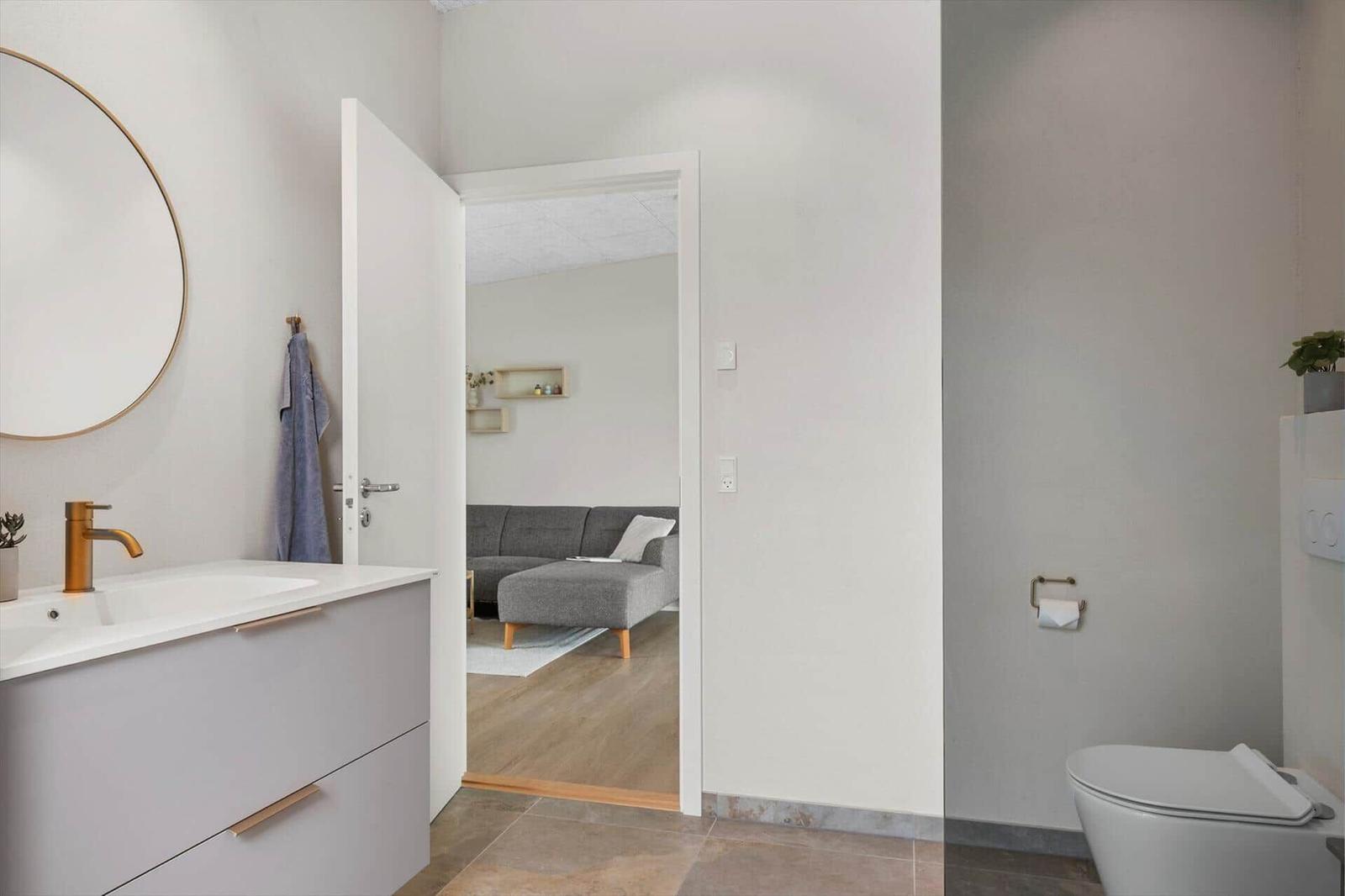 Badezimmer mit Waschtisch und Toilette, Blick in Wohnbereich mit Sofa.