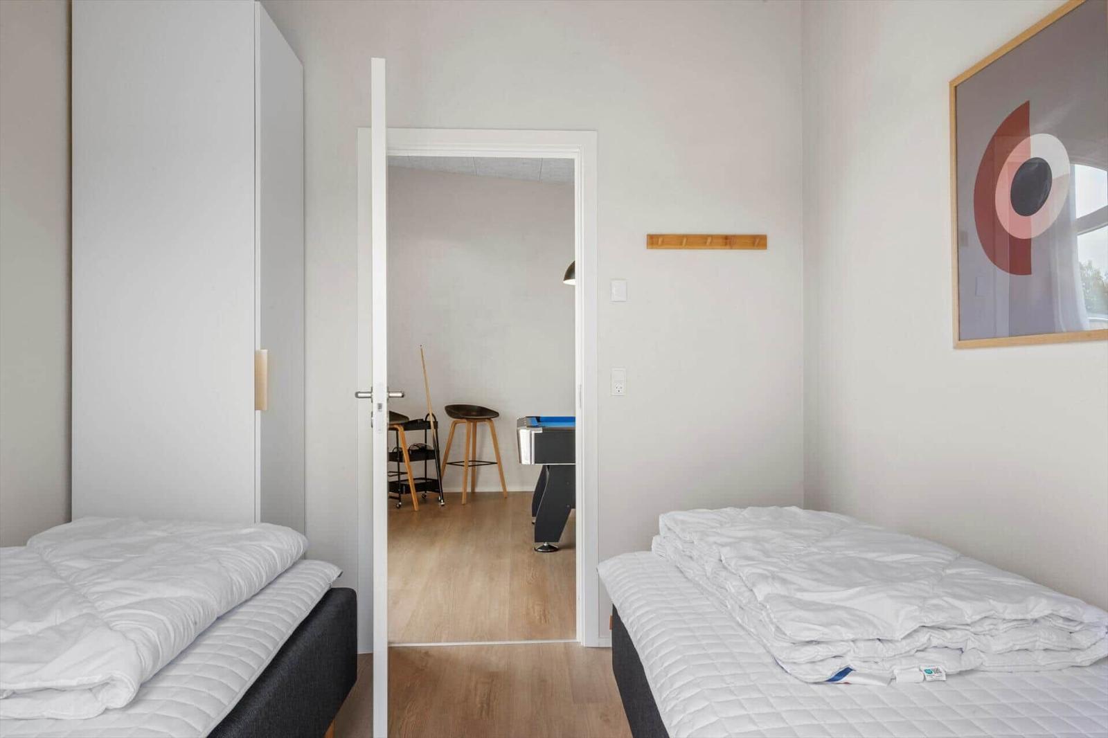 Zwei Schlafzimmer mit Matratzen und weißen Bettdecken. Durchgang zu einem Raum mit Tisch und Stühlen.