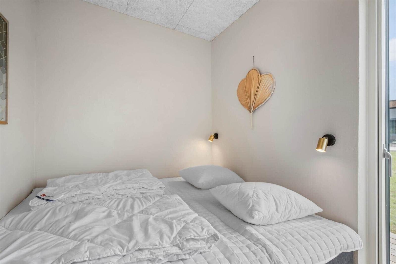 Schlafzimmer mit Bett, Wandlampe und Herzdekoration. Blick auf Balkon.