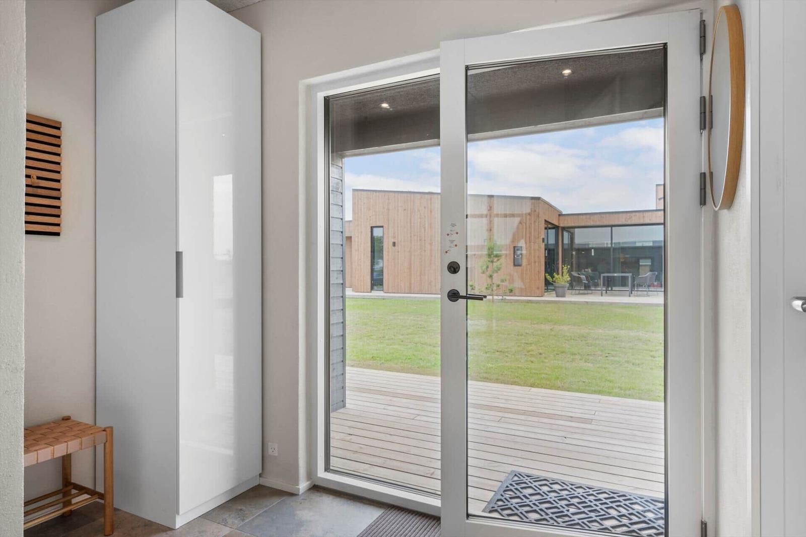 Durchgehende Glastür führt auf eine Terrasse mit Blick auf eine grüne Wiese und moderne Holzhäuser.