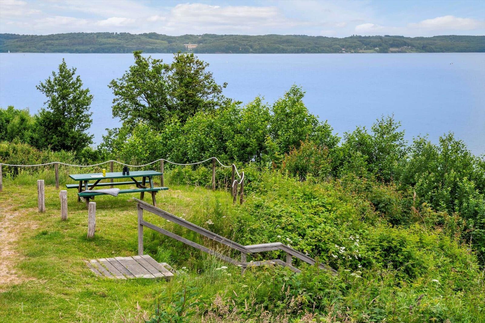 Grüner Picknickplatz mit Tisch und Bänken am Ufer eines Sees.