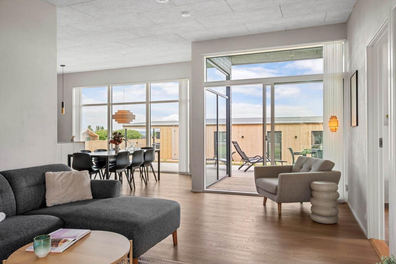 Wohn- und Essbereich mit großem Fenster und Terrasse. Möbel sind modern und minimalistisch.
