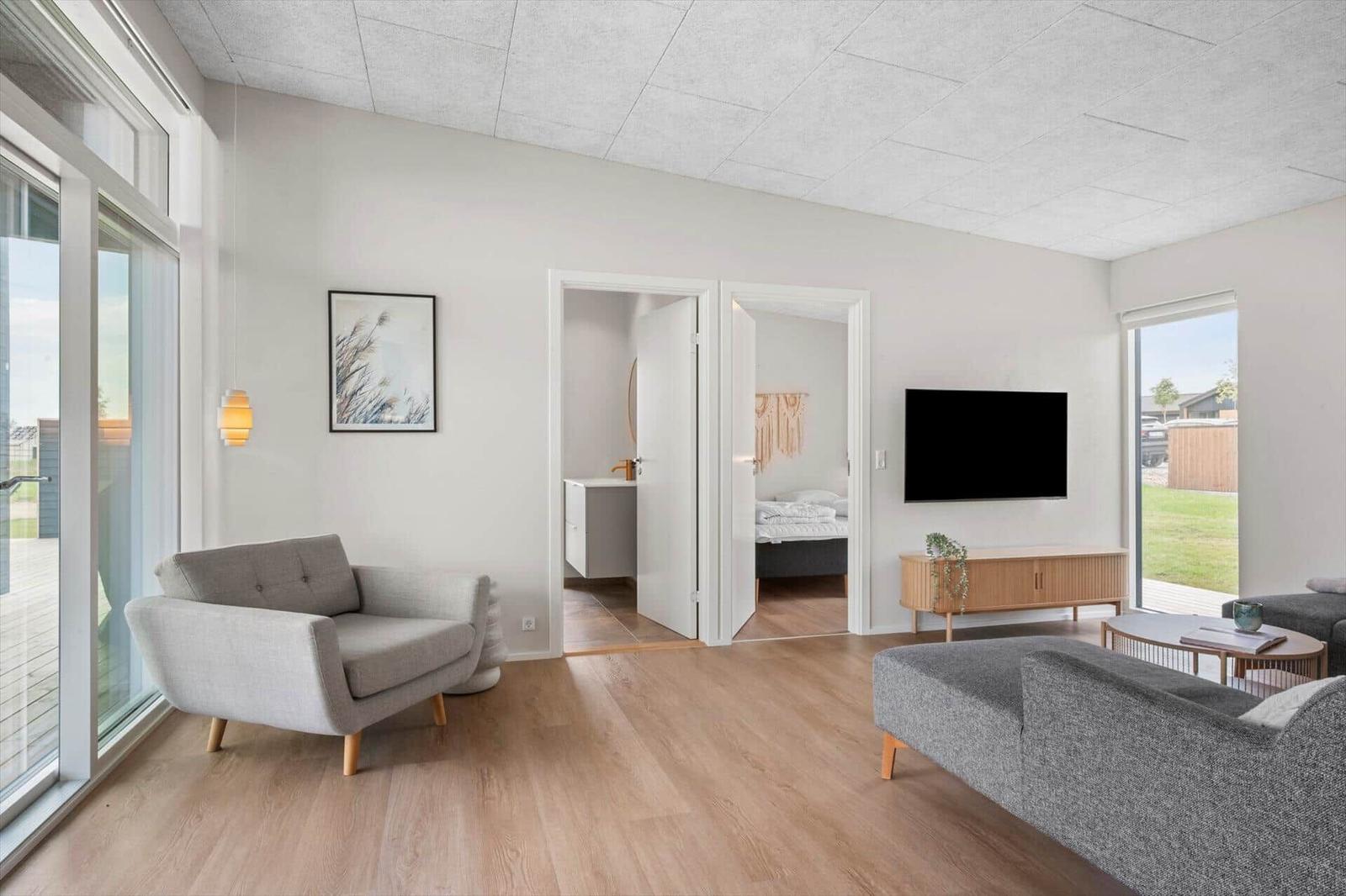 Wohnraum mit Sofa, Sessel, Fernseher und Blick auf den Garten.