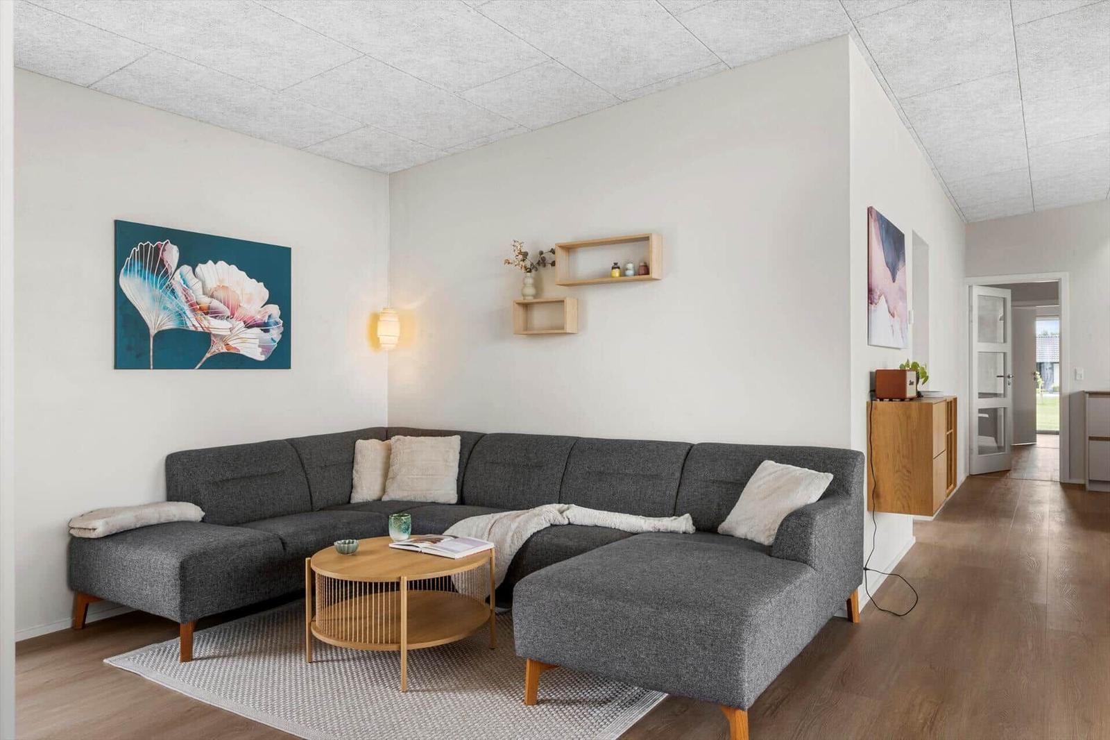 Ein Wohnzimmer mit grauem Sofa, Holztisch und Wandbildern.