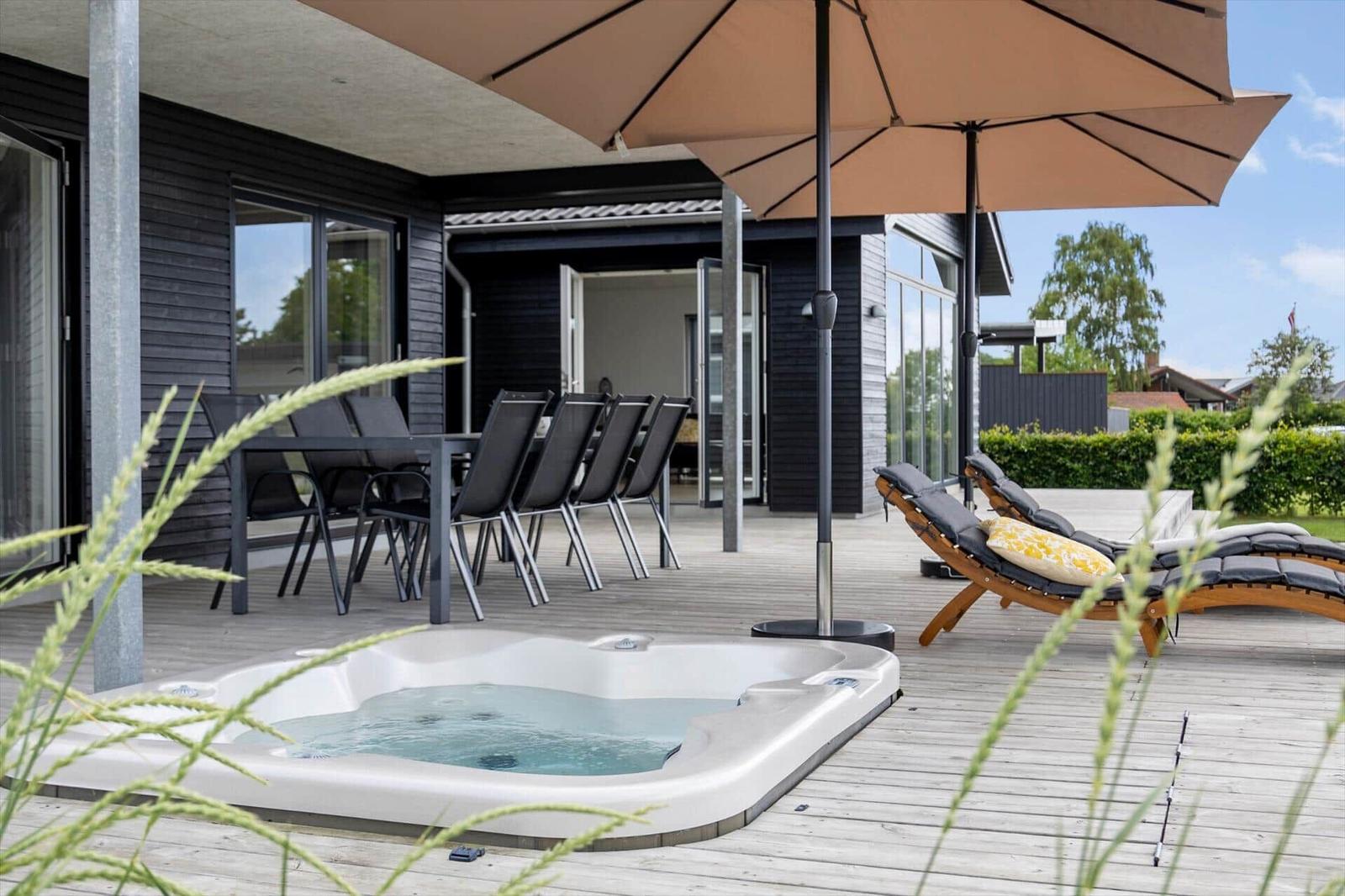 Outdoor area with hot tub, umbrella, and lounge chairs on wooden deck.