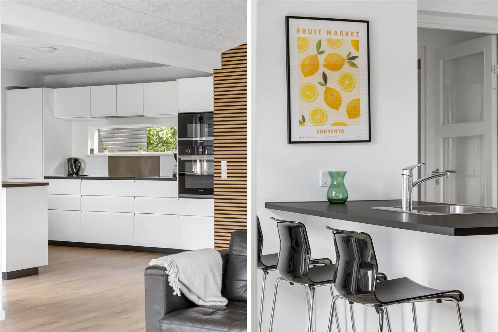 Modern kitchen with white cabinets and kitchen island. Bar stools and wall art are visible.