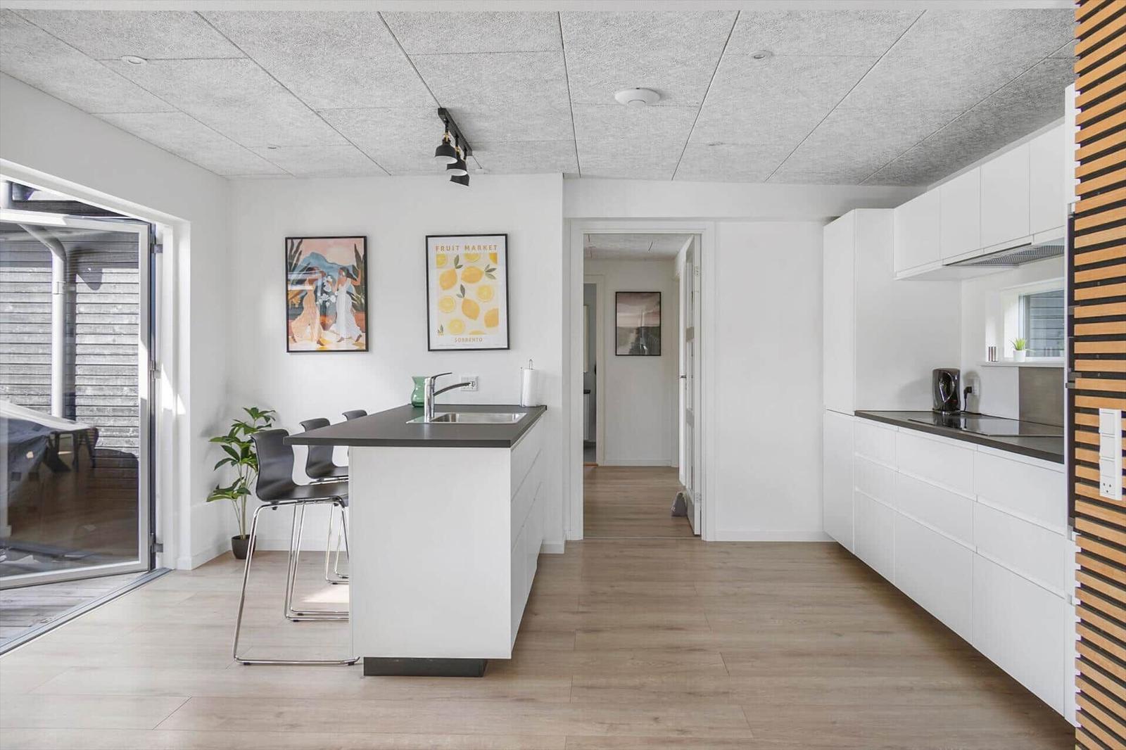 Kitchen with dining area, white cabinets, and wooden floor. Hallway to the apartment.