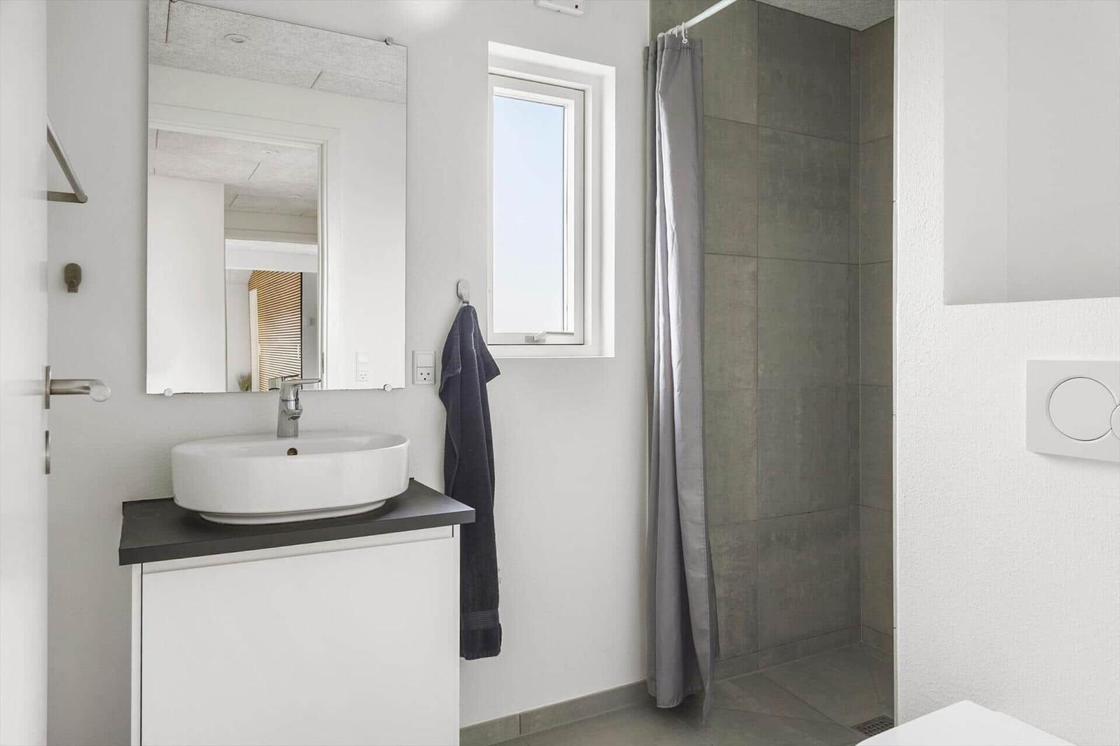 Bathroom with sink, mirror, shower, and window.