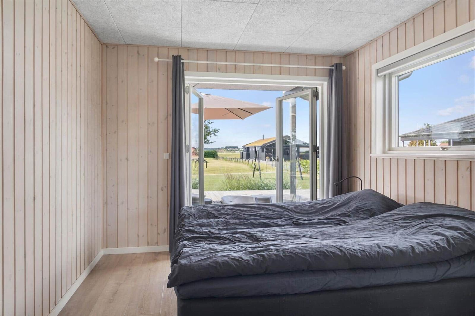 Bedroom with view of garden and terrace. Wooden walls and large windows.