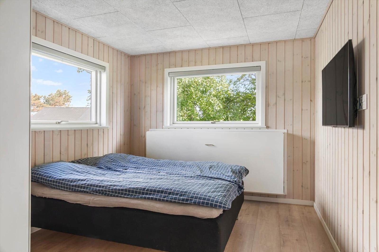 Bedroom with bed, two windows, and wall-mounted TV.